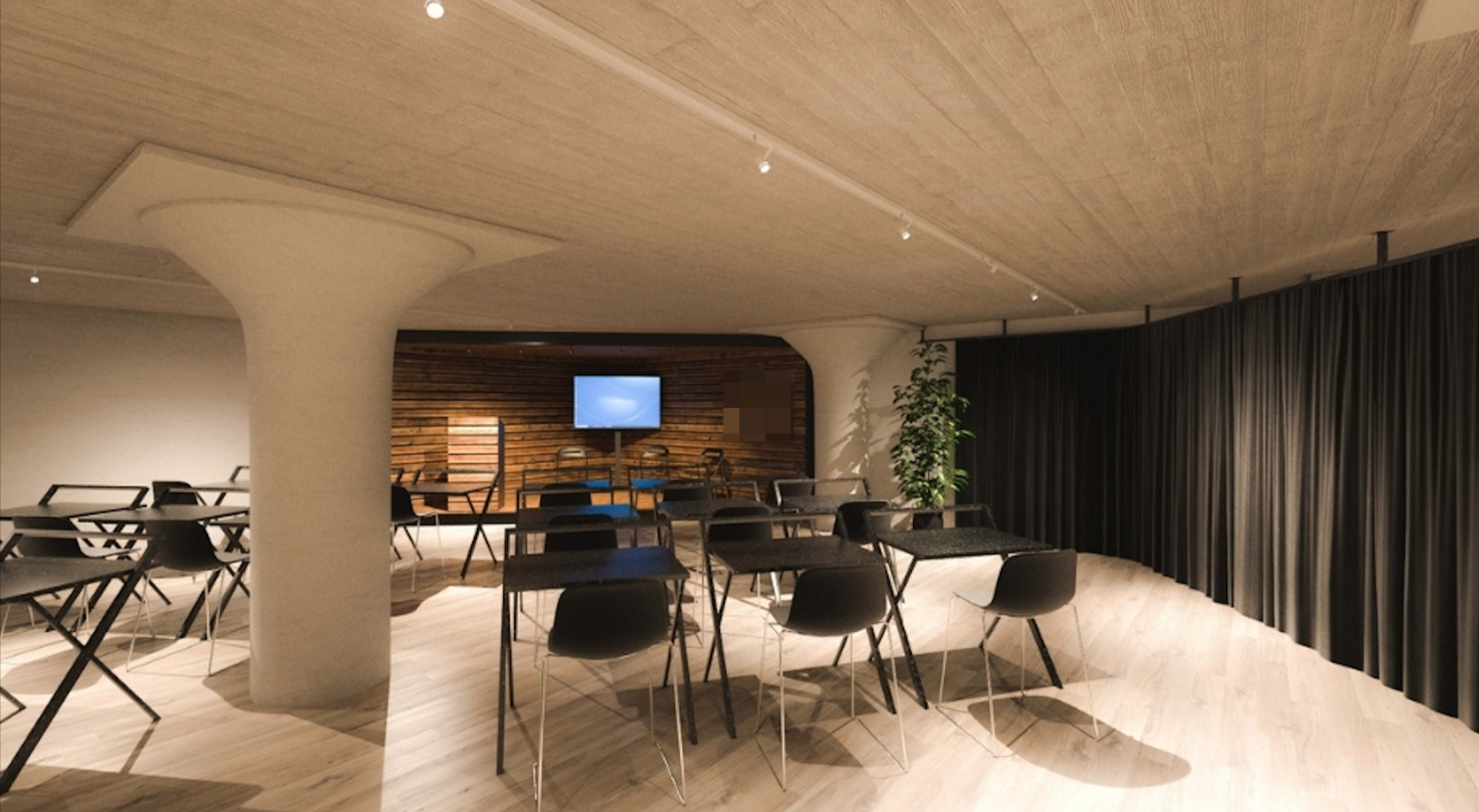 A modern, open classroom or meeting space with multiple black folding tables and chairs arranged in rows, along with a television mounted on a wood-paneled wall.