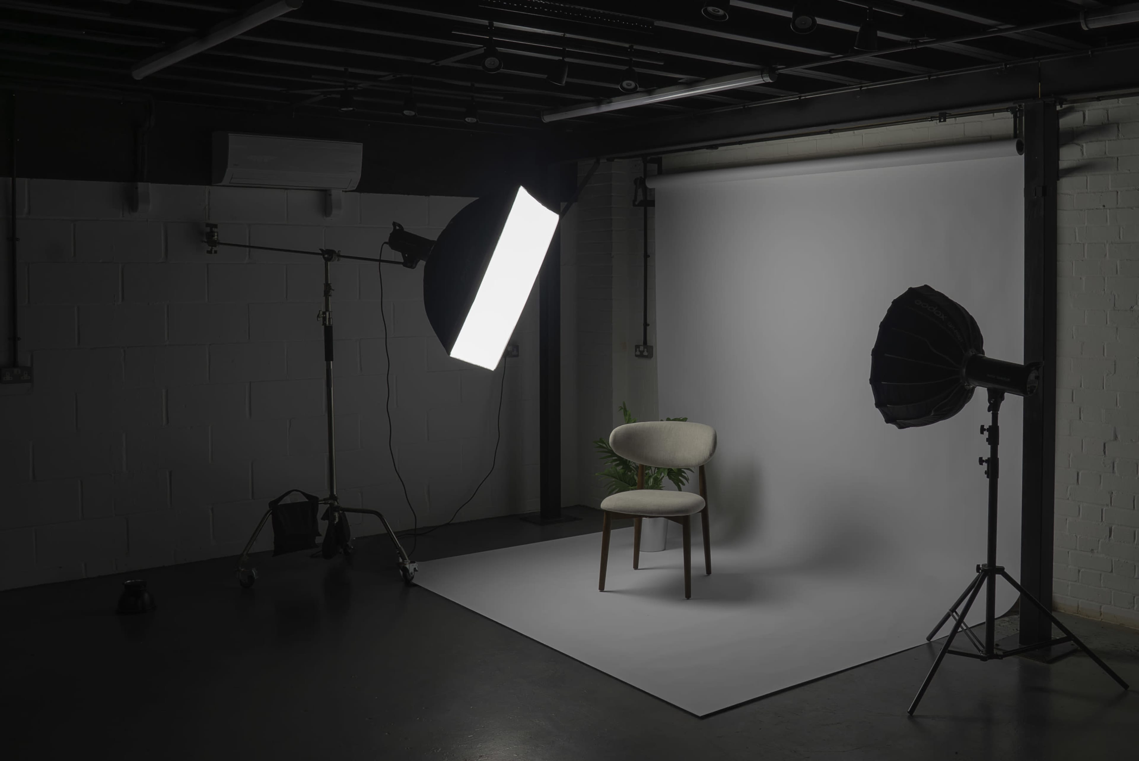 The image depicts a photography studio with a chair positioned on a white backdrop, illuminated by two lighting setups.