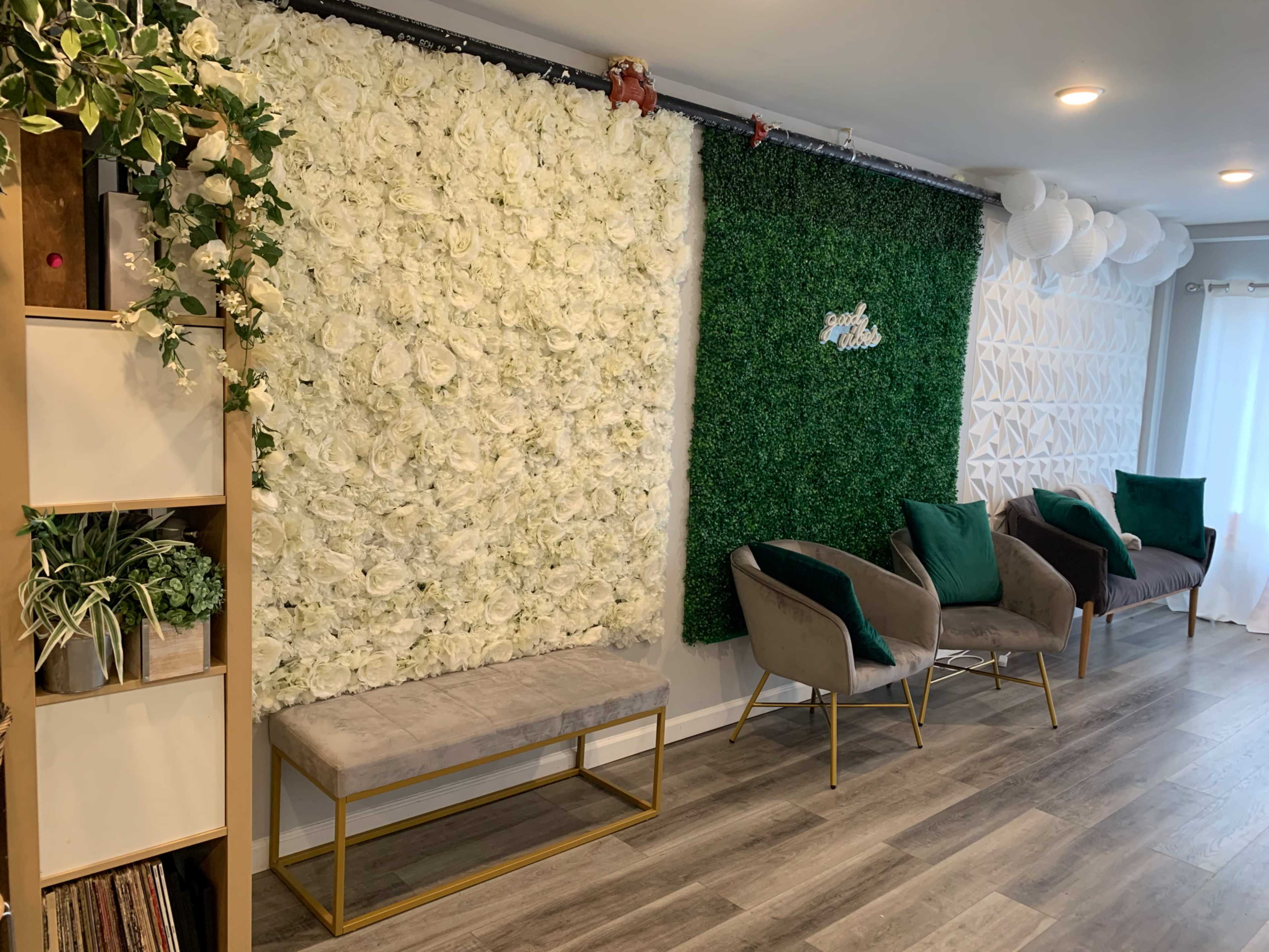 A stylish interior featuring a wall of white flowers, a green artificial grass wall, and modern seating in a well-lit space.