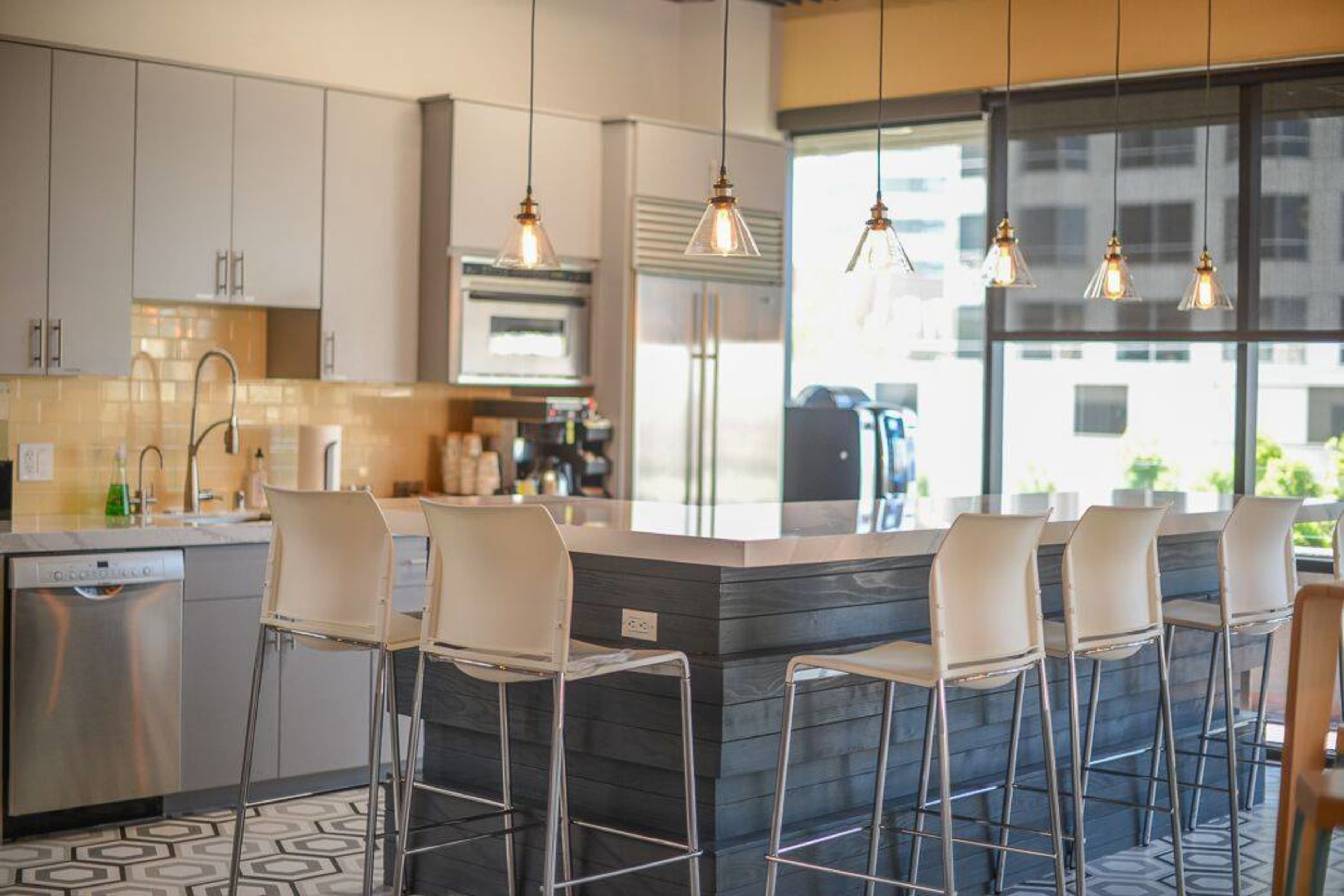 A modern kitchen features a large island with bar seating and pendant lights above, along with stainless steel appliances and large windows.
