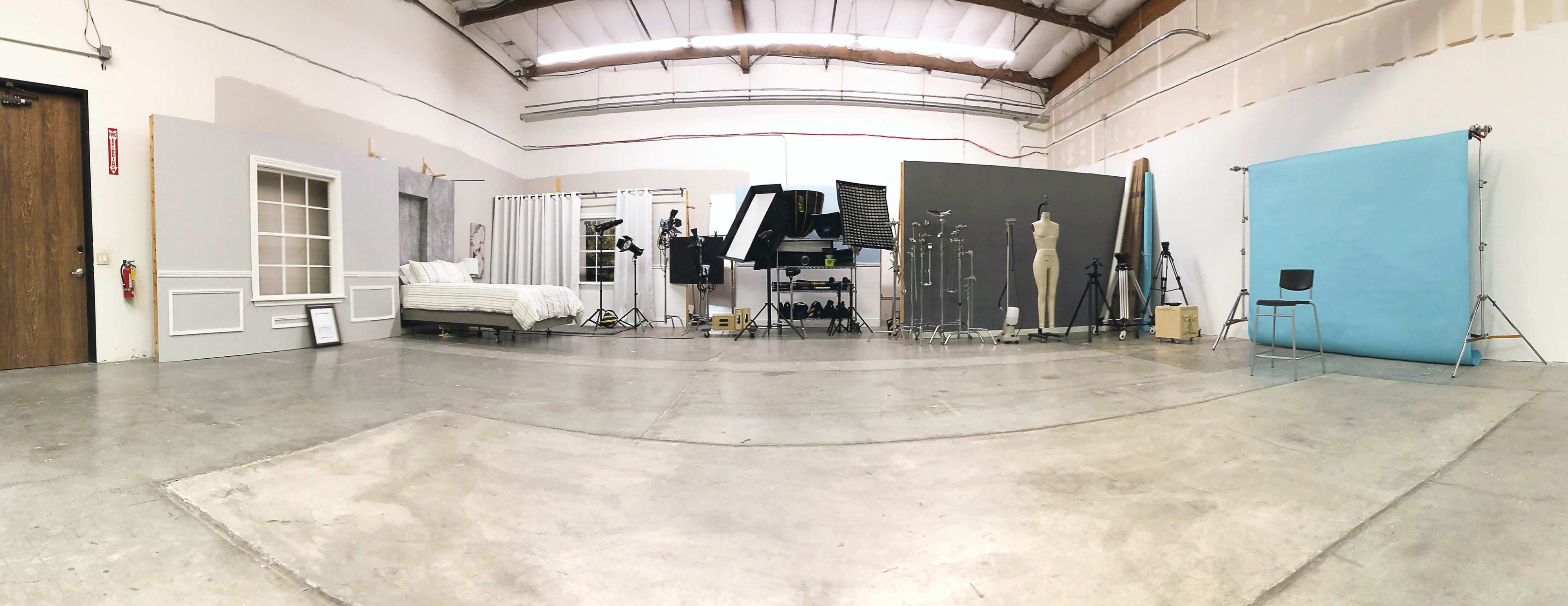 A spacious photography studio with various backdrops, lighting equipment, and a bed set up against one wall.