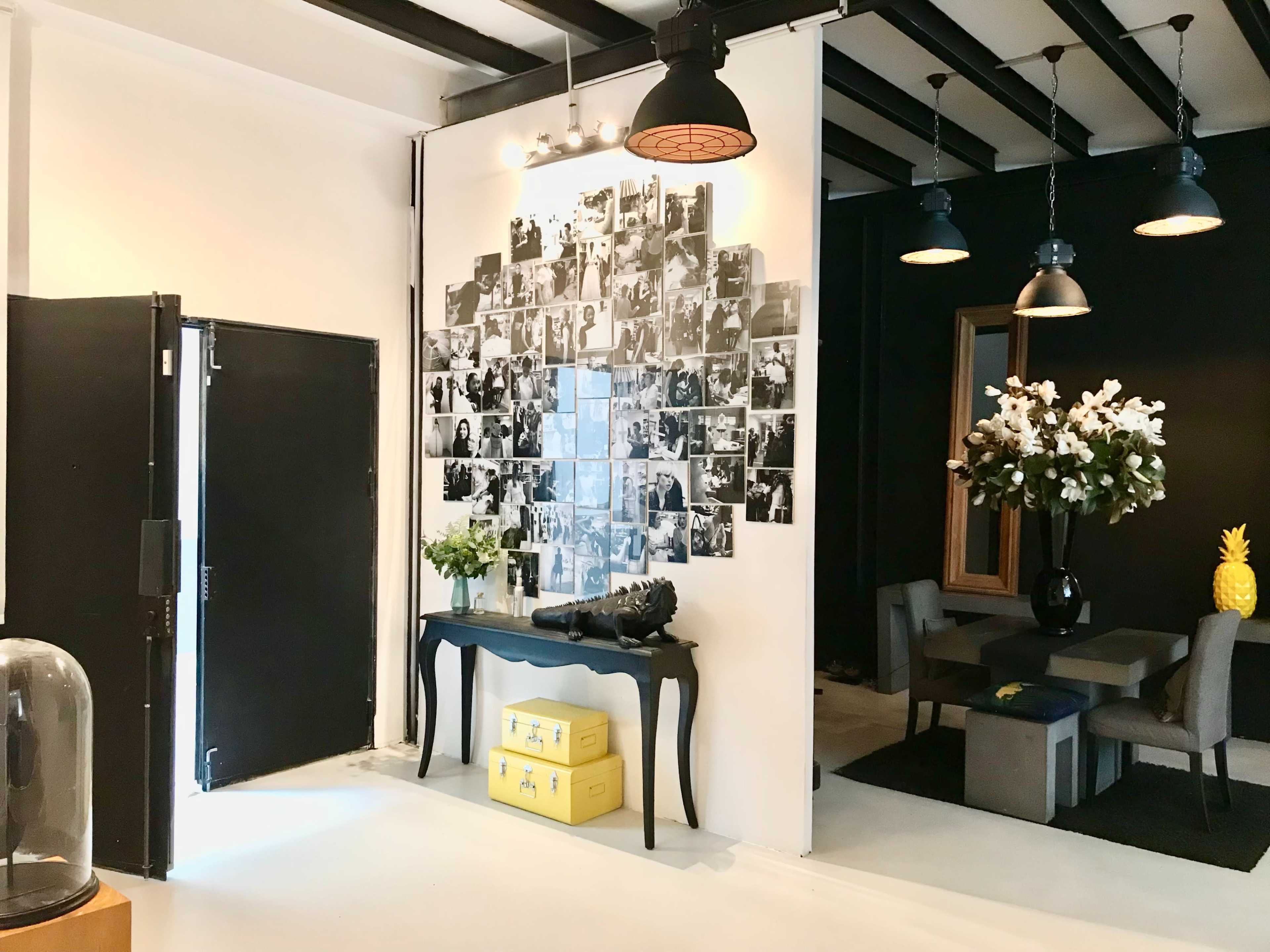 A stylish interior space featuring a black and white photo wall, a decorative table with a camera on it, and a dining area with floral arrangements and a pineapple centerpiece.
