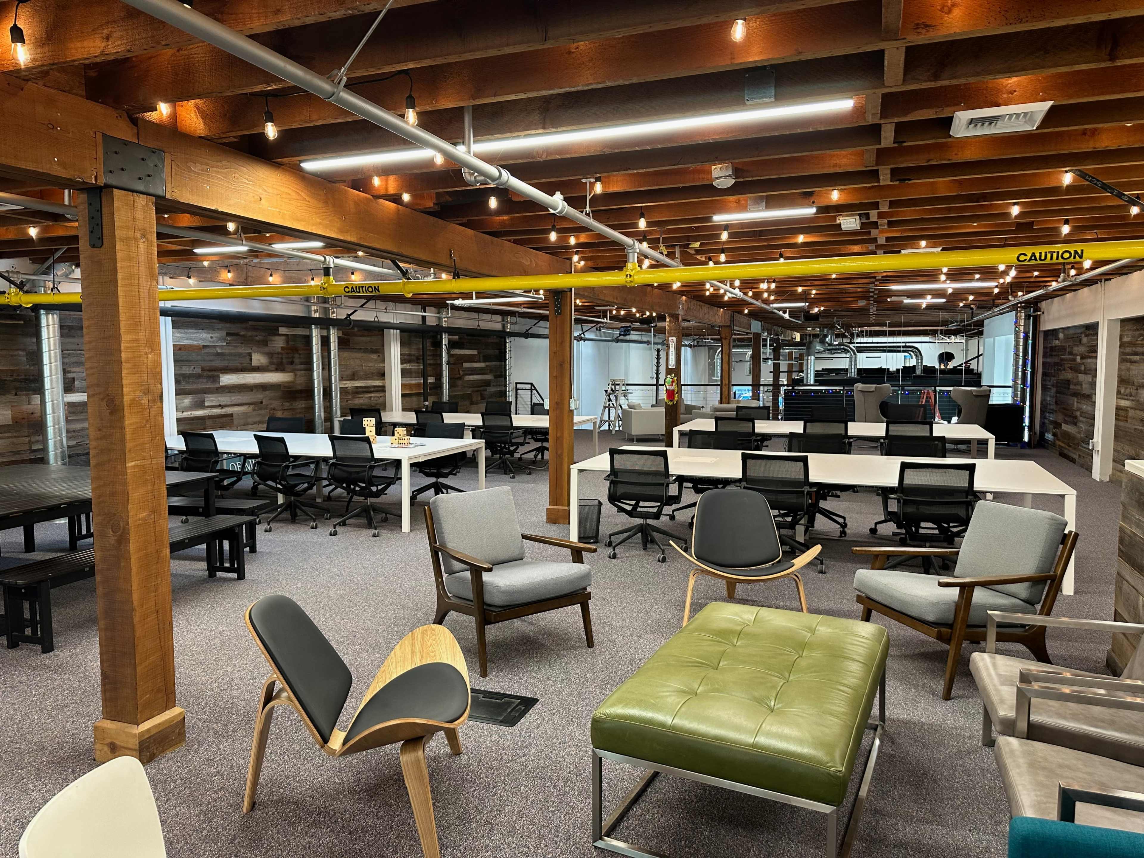 A modern office space with wooden beams, various seating arrangements, and workstations set up in a spacious layout.