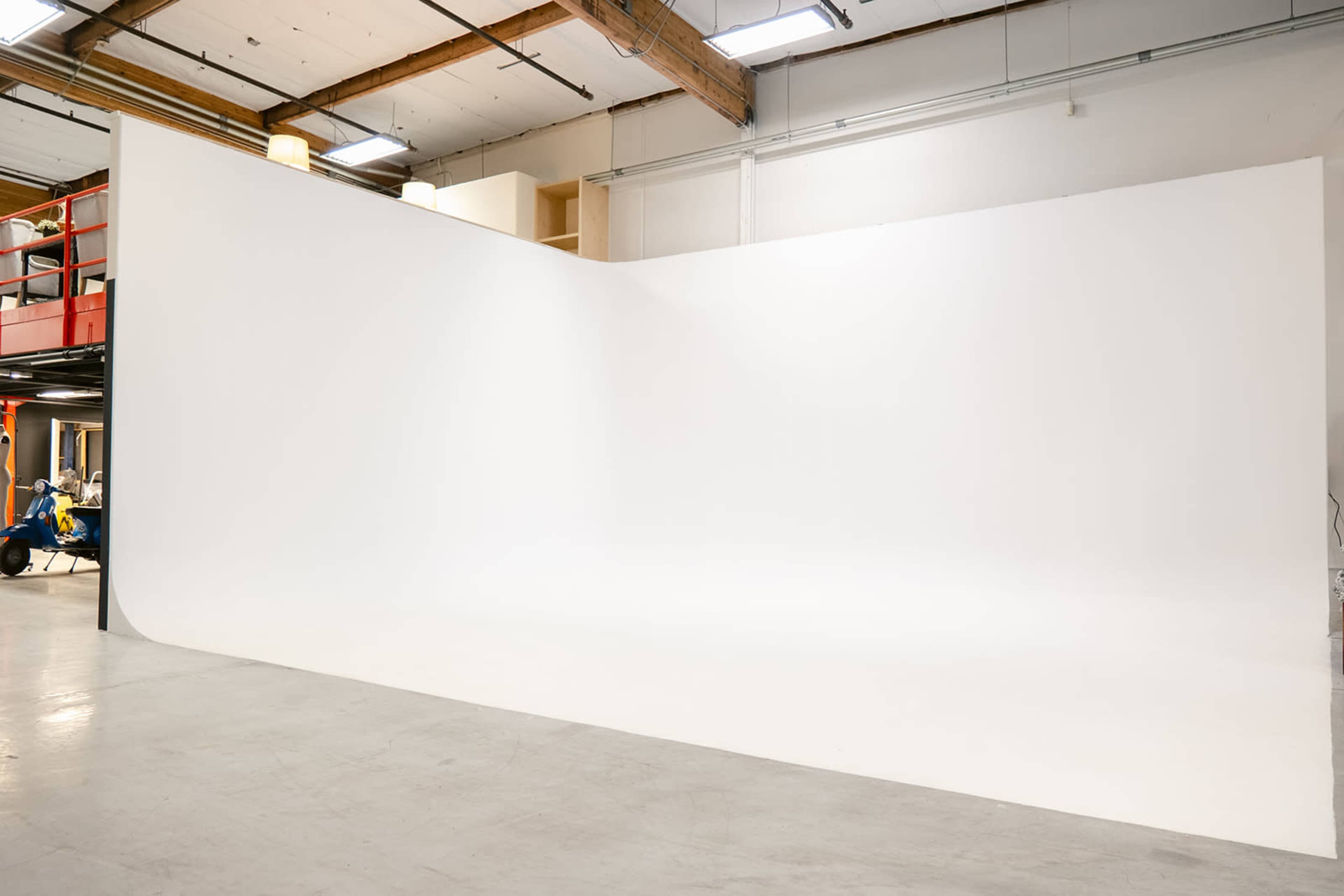 The image shows a spacious studio with a large, seamless white backdrop and a concrete floor.