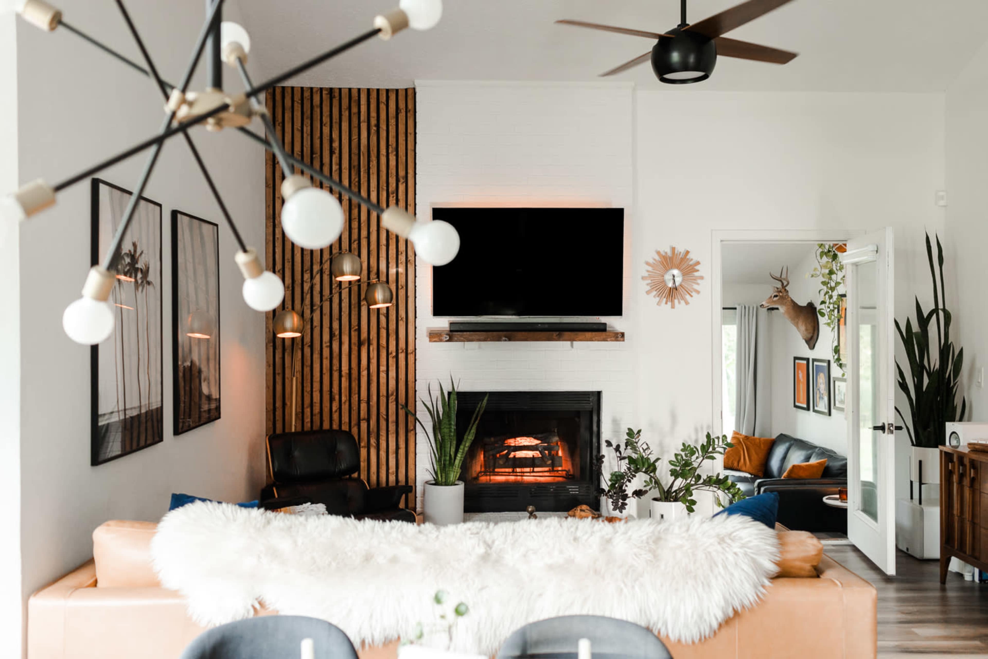 A modern living room features a brown leather sofa, a fireplace with a mounted TV above, and decorative plants amidst a backdrop of wood paneling and wall art.