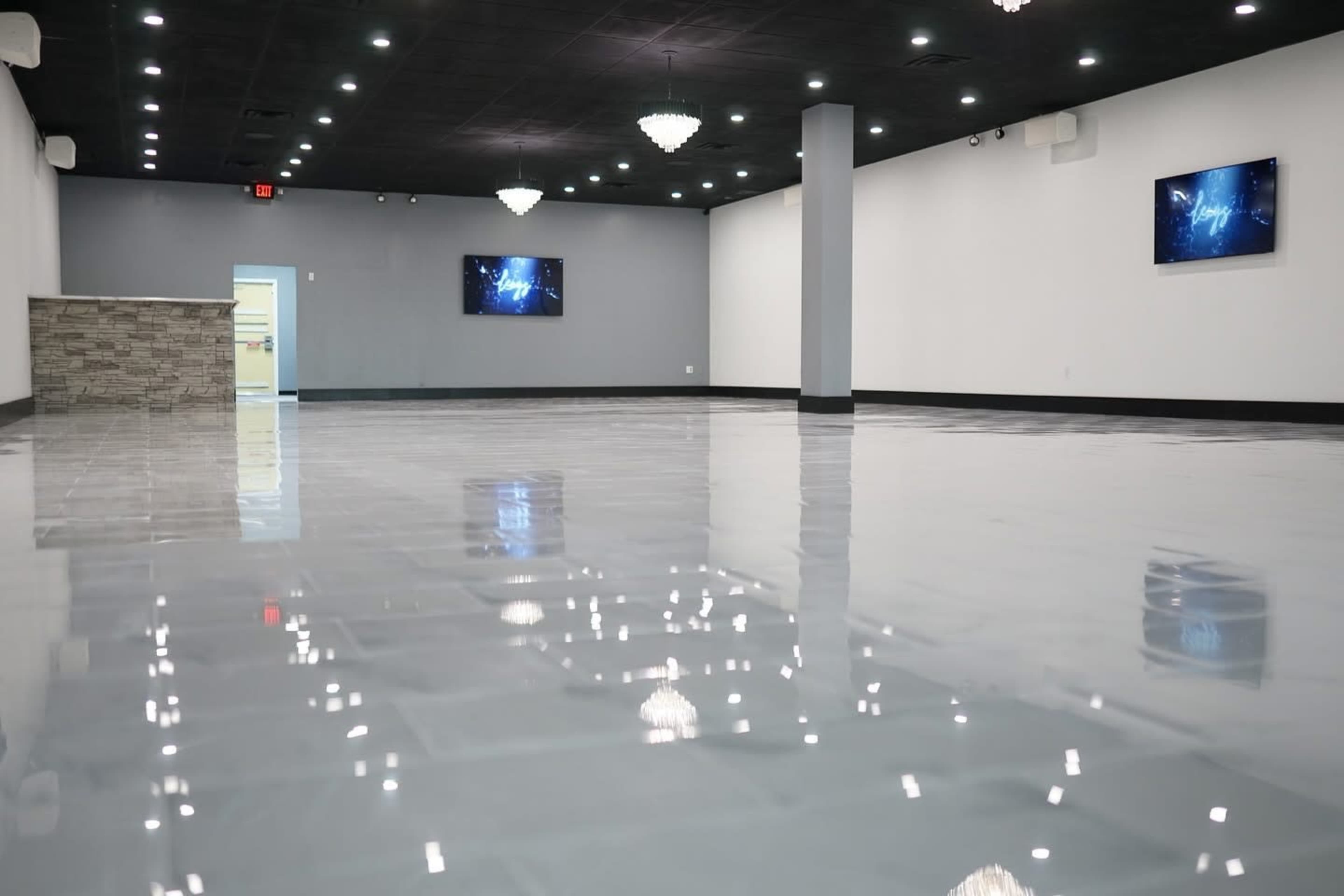 The image shows an empty, modern interior space with glossy tiled flooring, two wall-mounted screens, and crystal chandeliers hanging from the ceiling.