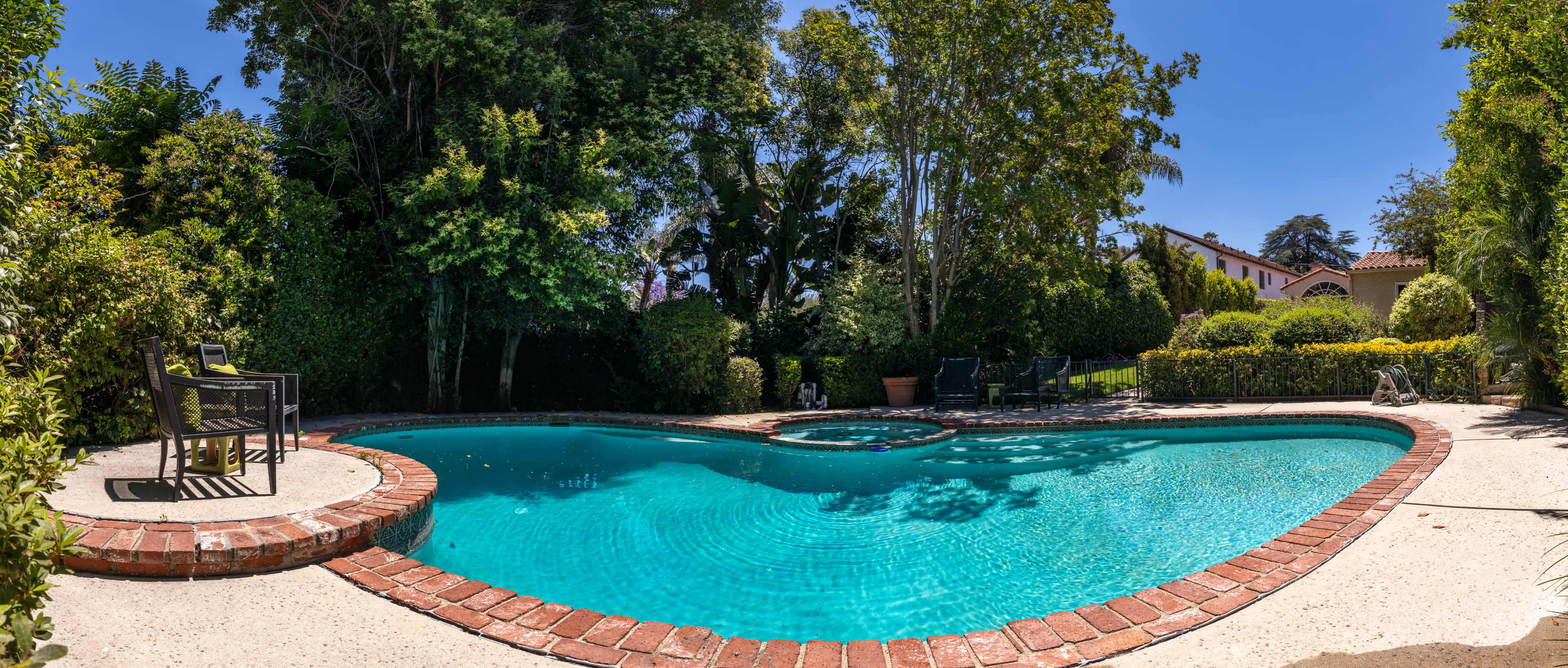 The image shows a heart-shaped swimming pool surrounded by lush greenery and patio seating.