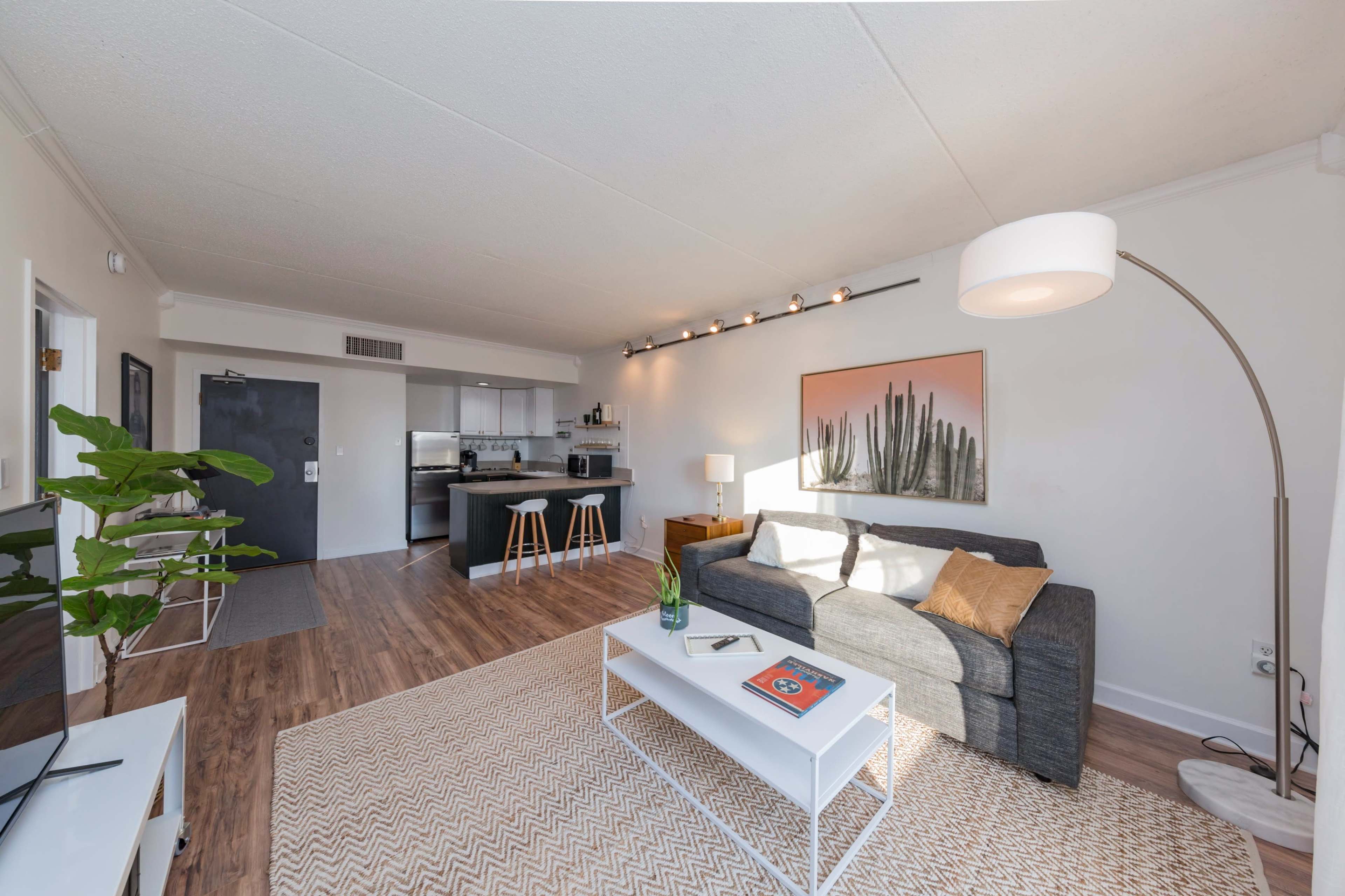 A modern living room with a gray sofa, a white coffee table, and a small kitchen area in the background.