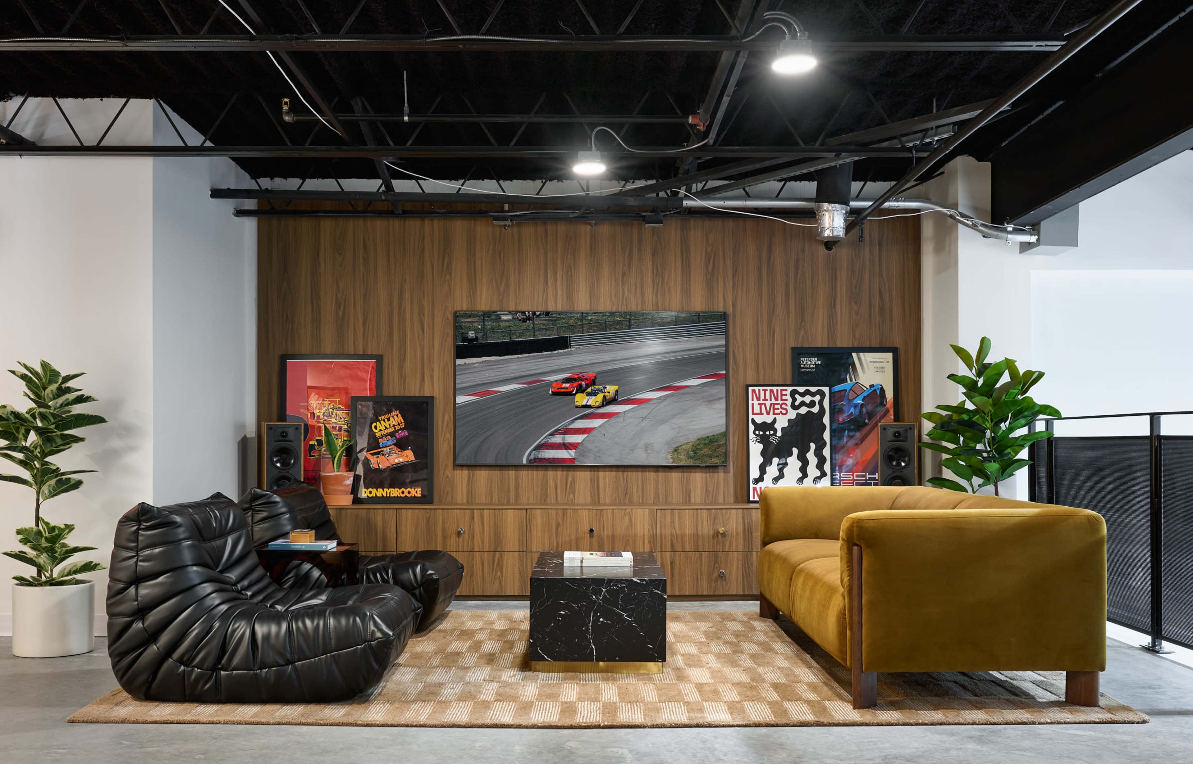 The image shows a modern living room with a dark wood accent wall, featuring a large television mounted above a sleek cabinet, surrounded by colorful artwork and plants, along with plush seating arrangements.