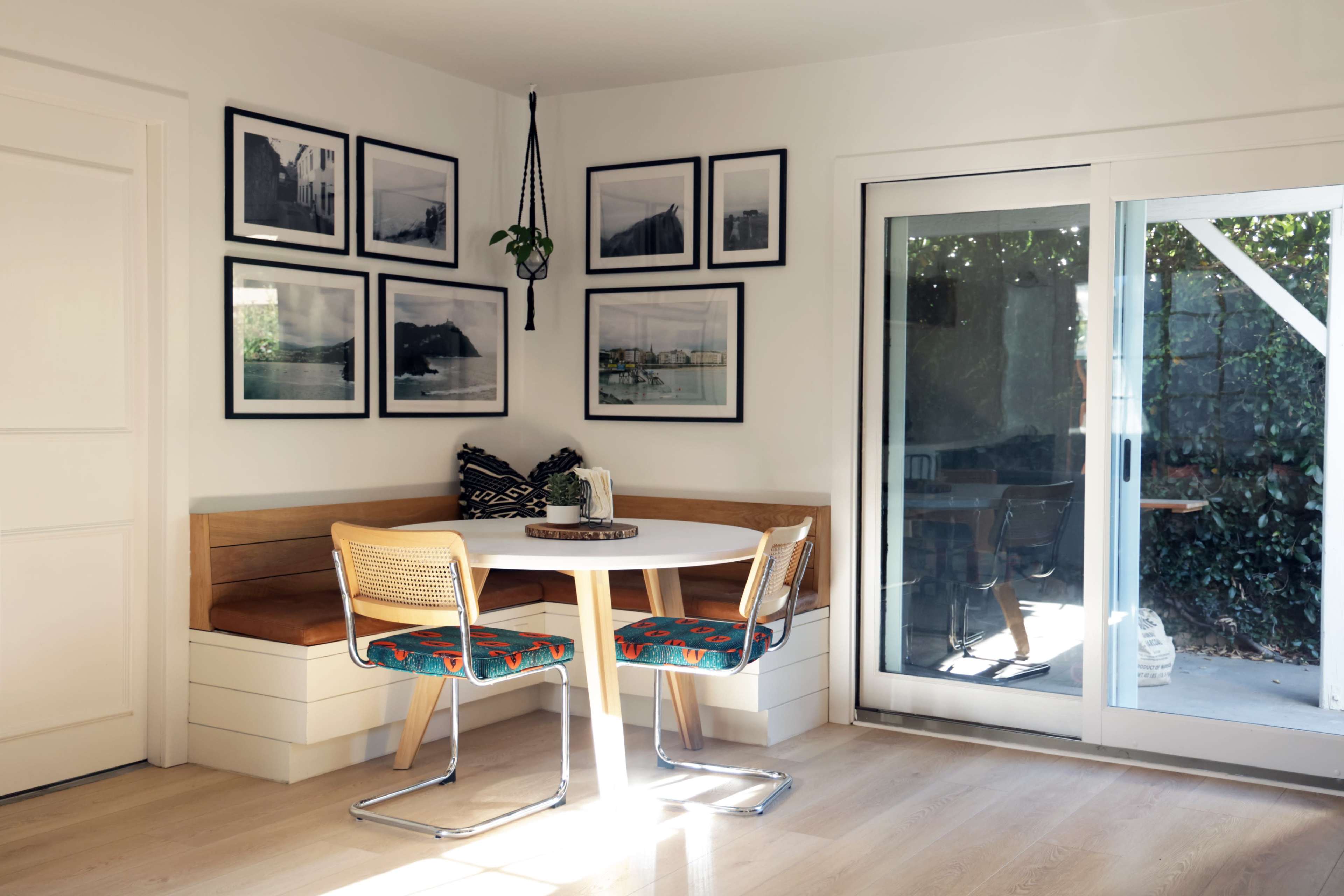 A small dining area features a round table surrounded by two chairs, with a built-in bench and framed photographs on the walls.