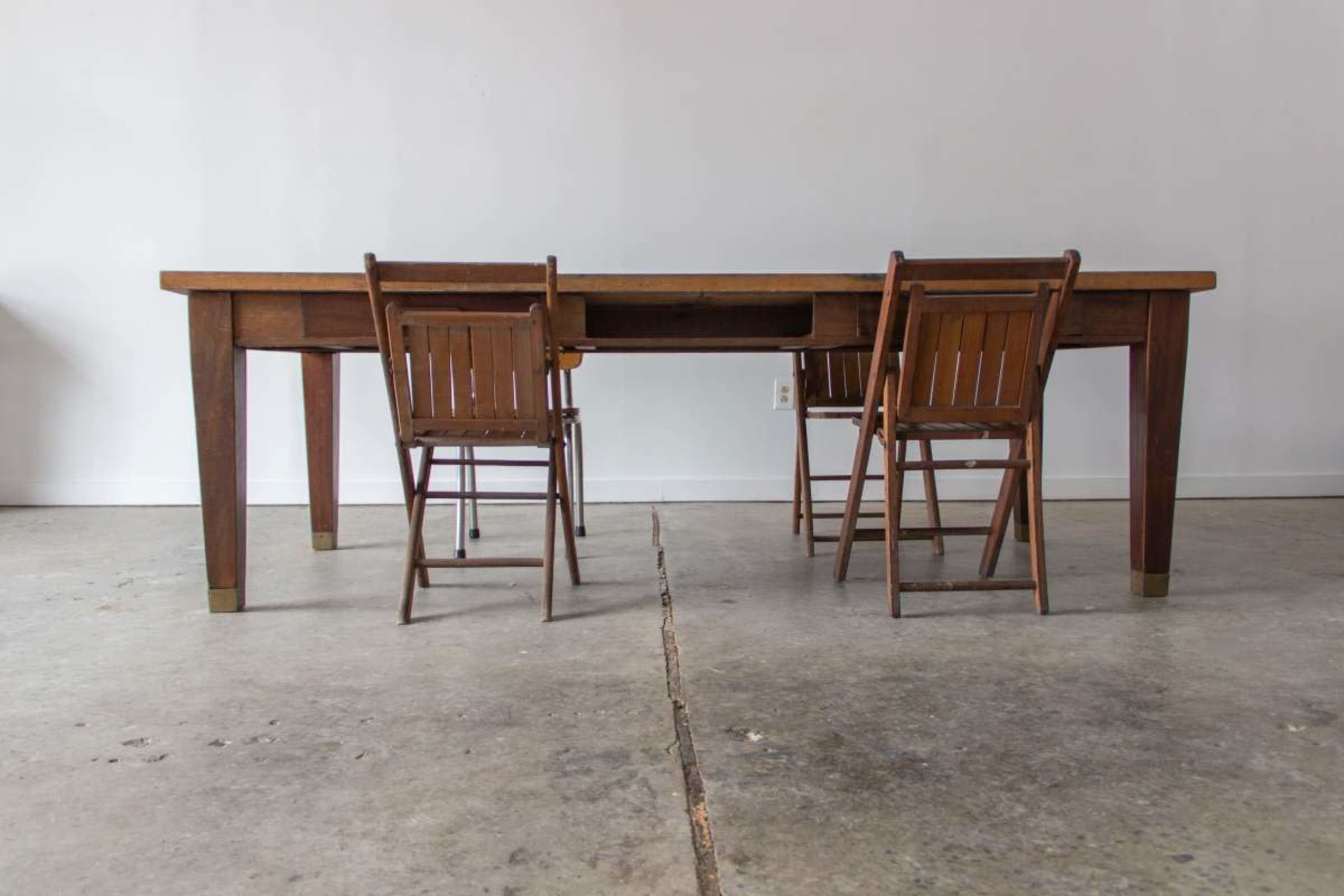 A wooden table with two wooden folding chairs is positioned on a concrete floor in a minimalist room.