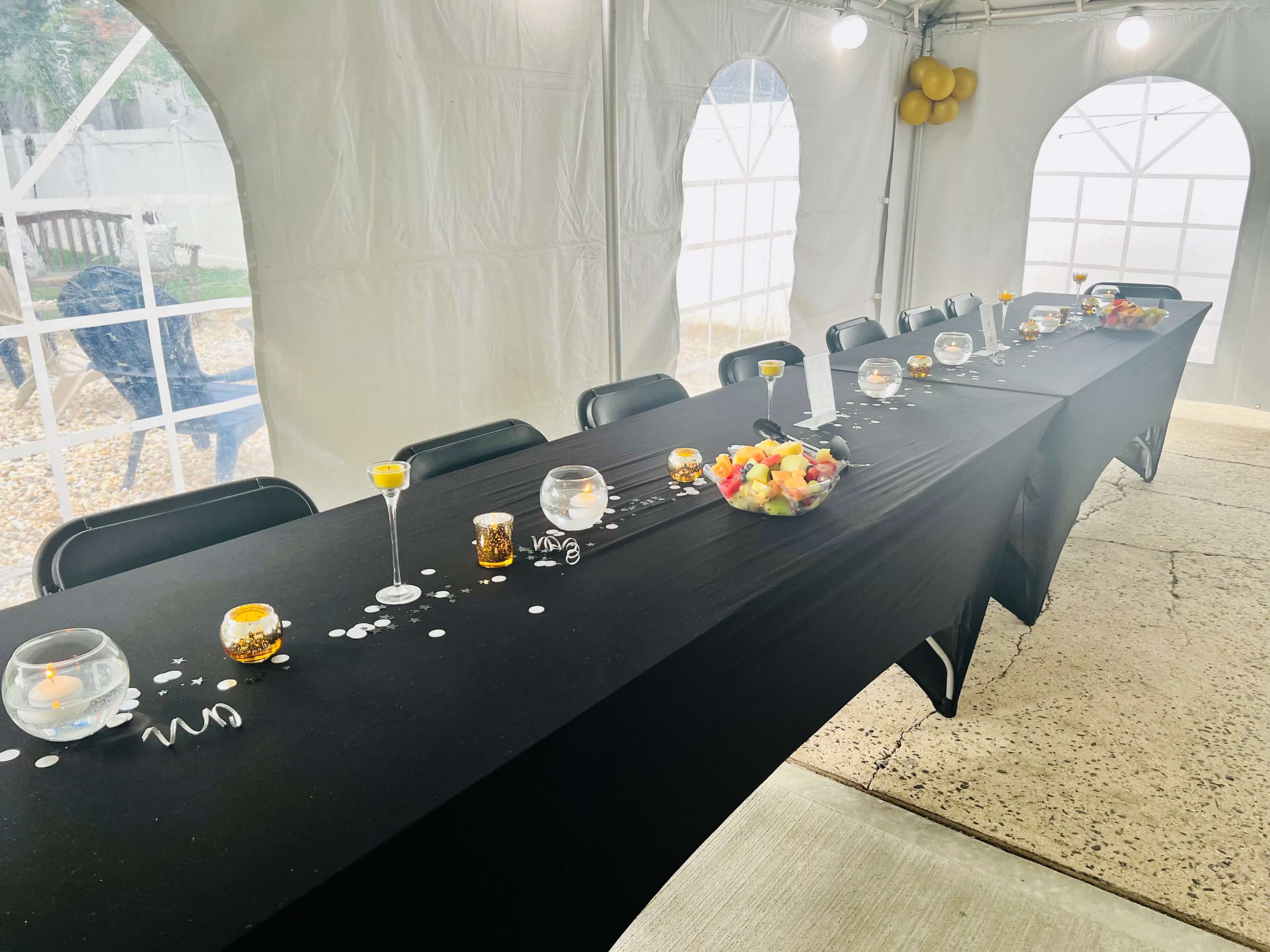 A long, black table is set inside a tent, adorned with decorative bowls and candles, with additional decorations placed along the center.