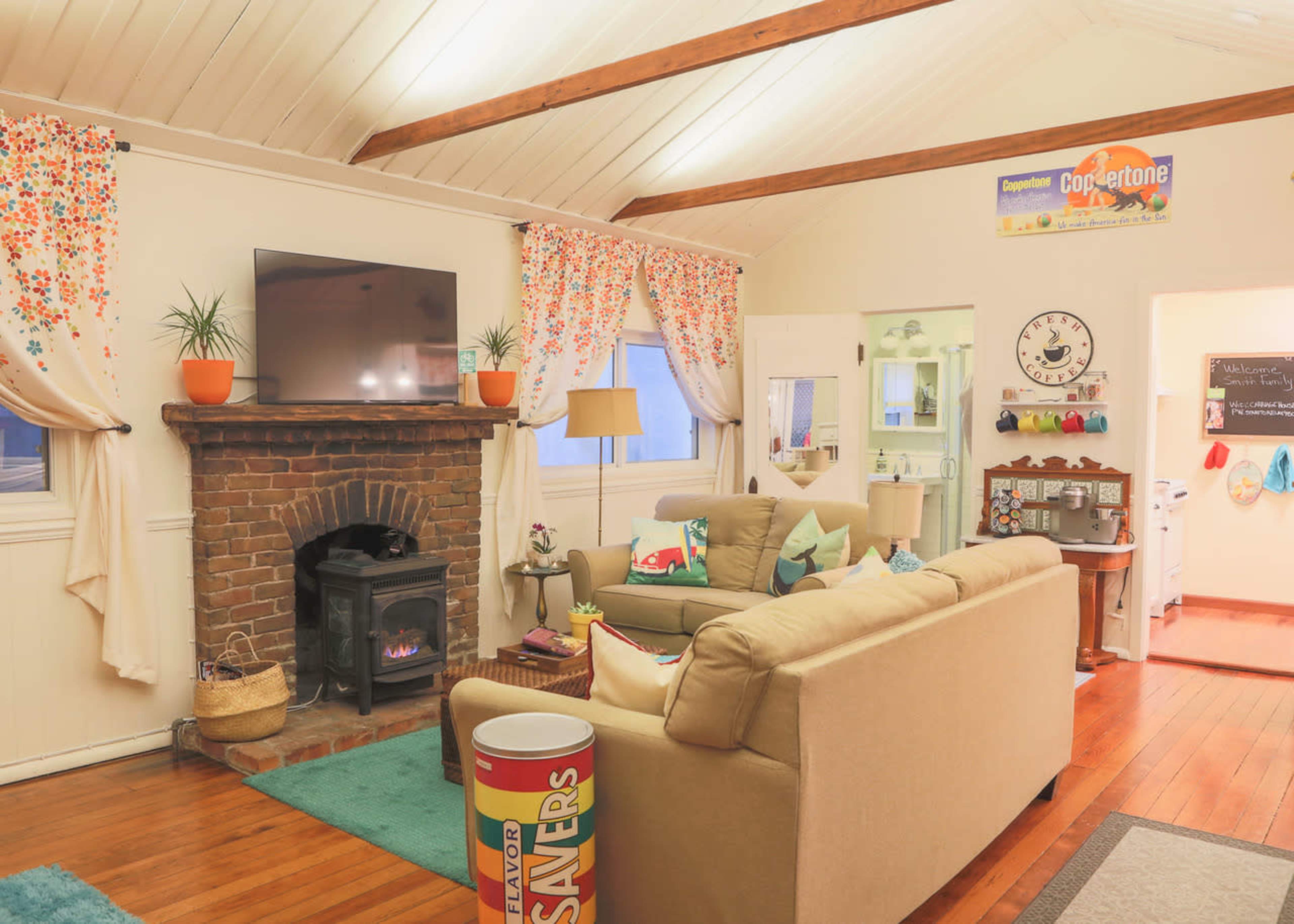 A cozy living room with a brick fireplace, a television mounted on the wall, and a sofa arranged around a small table.