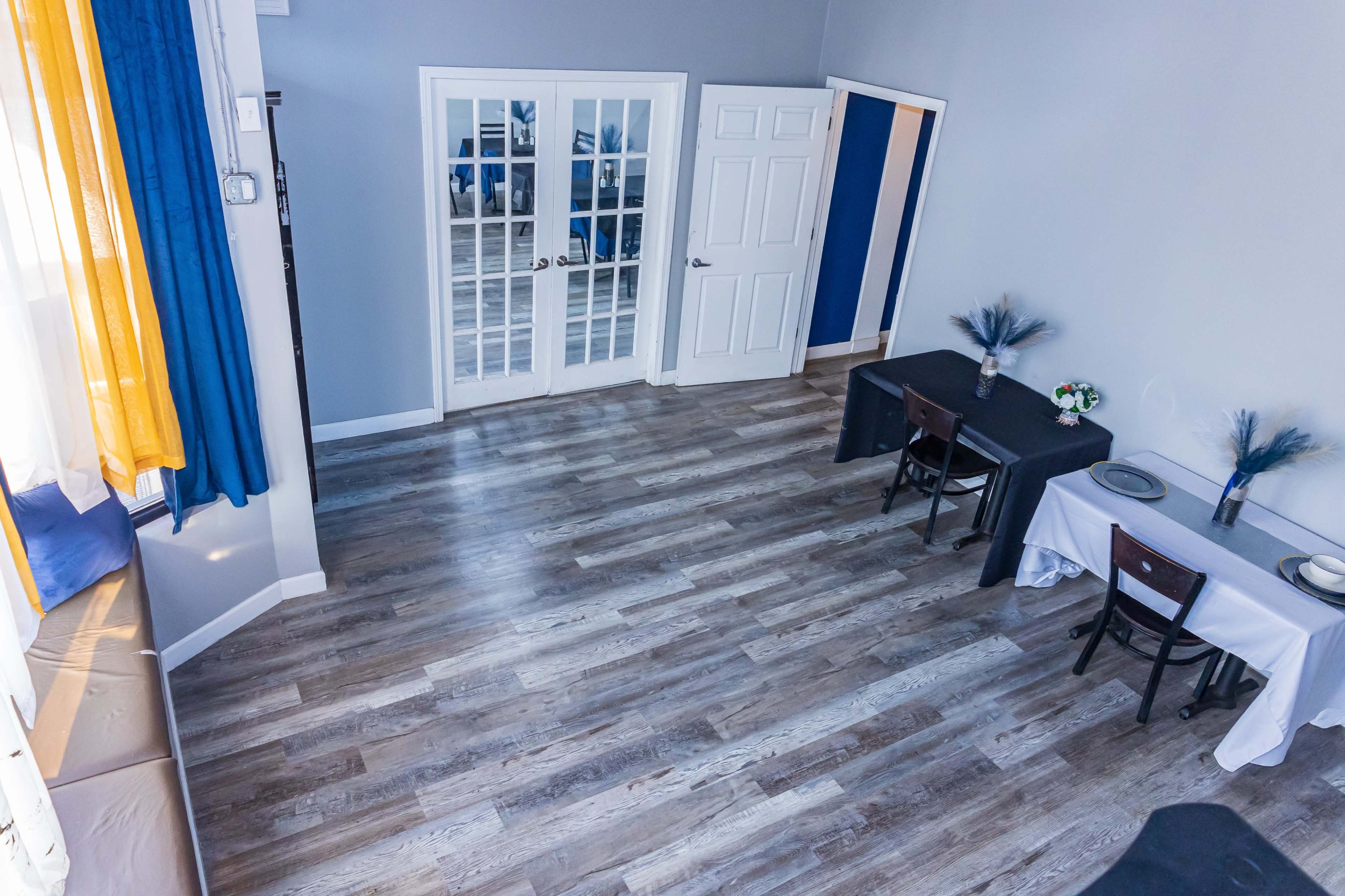 The image shows a spacious room with two tables set up, one black and one white, and a set of double doors leading to another area.