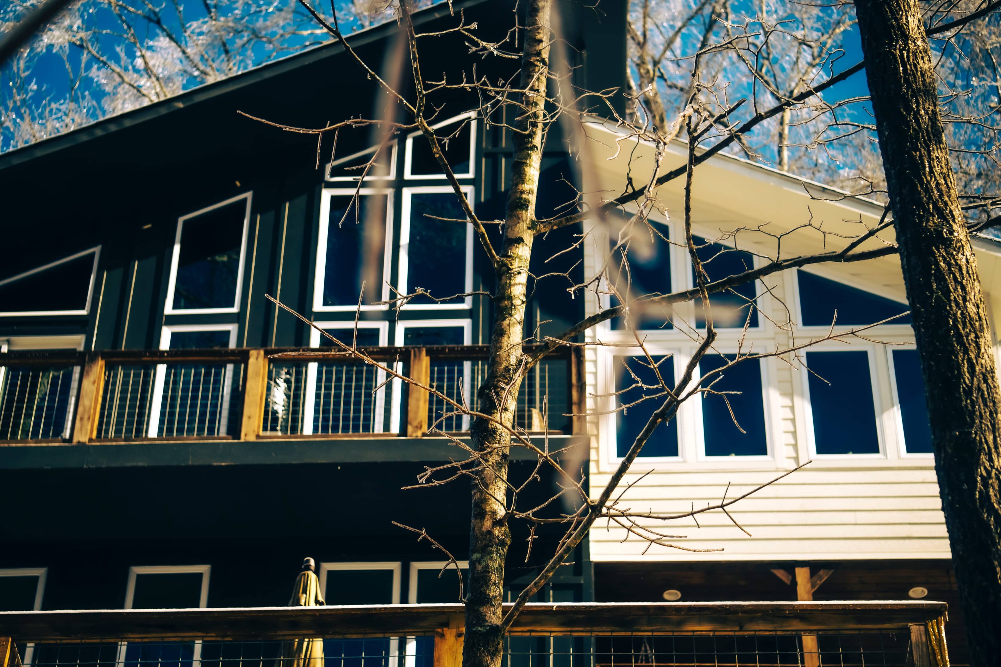 A modern house features two distinct architectural styles with large windows and a balcony, surrounded by bare trees.
