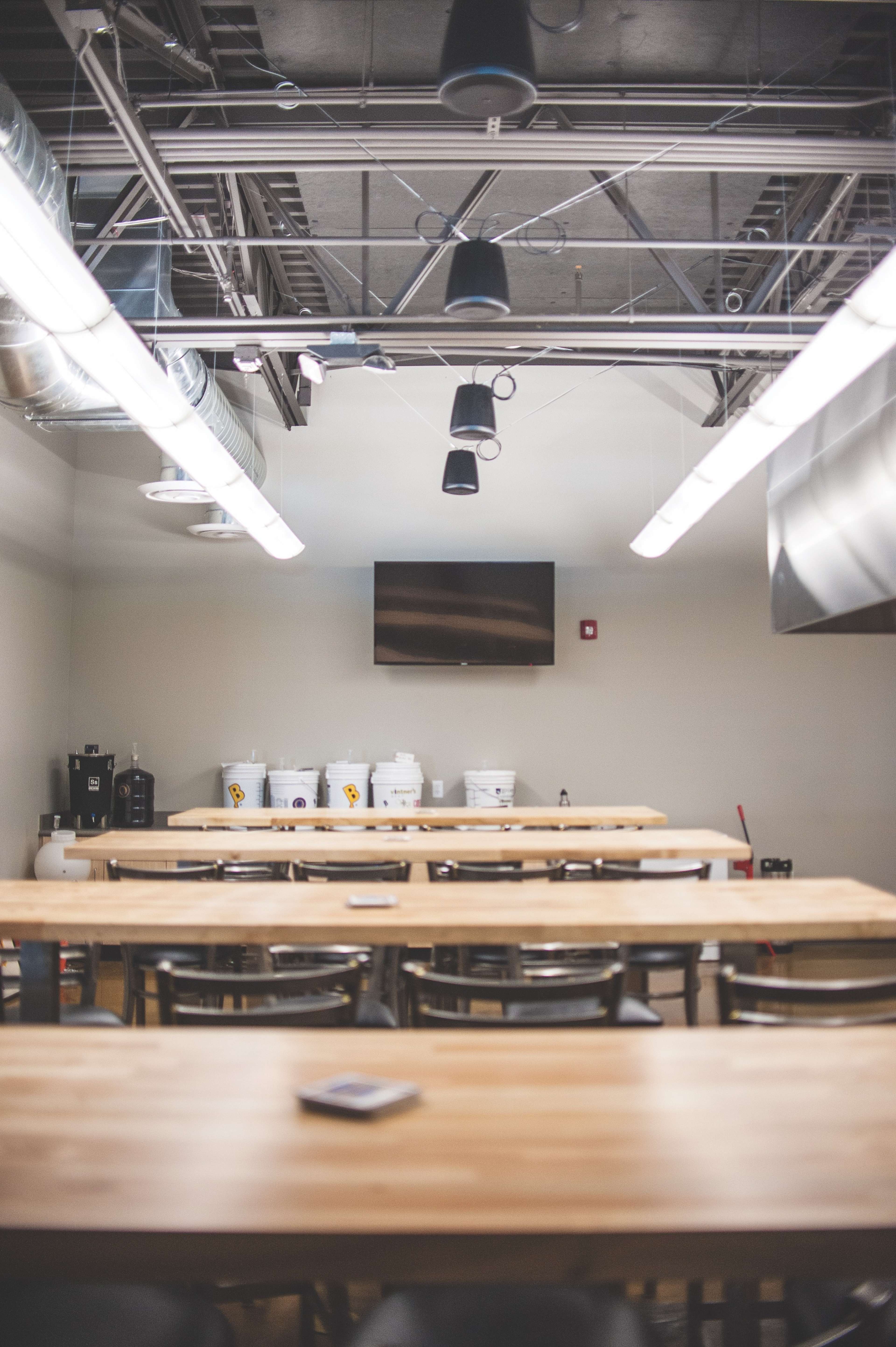 A spacious, modern kitchen area with multiple wooden tables and a wall-mounted television in the background.