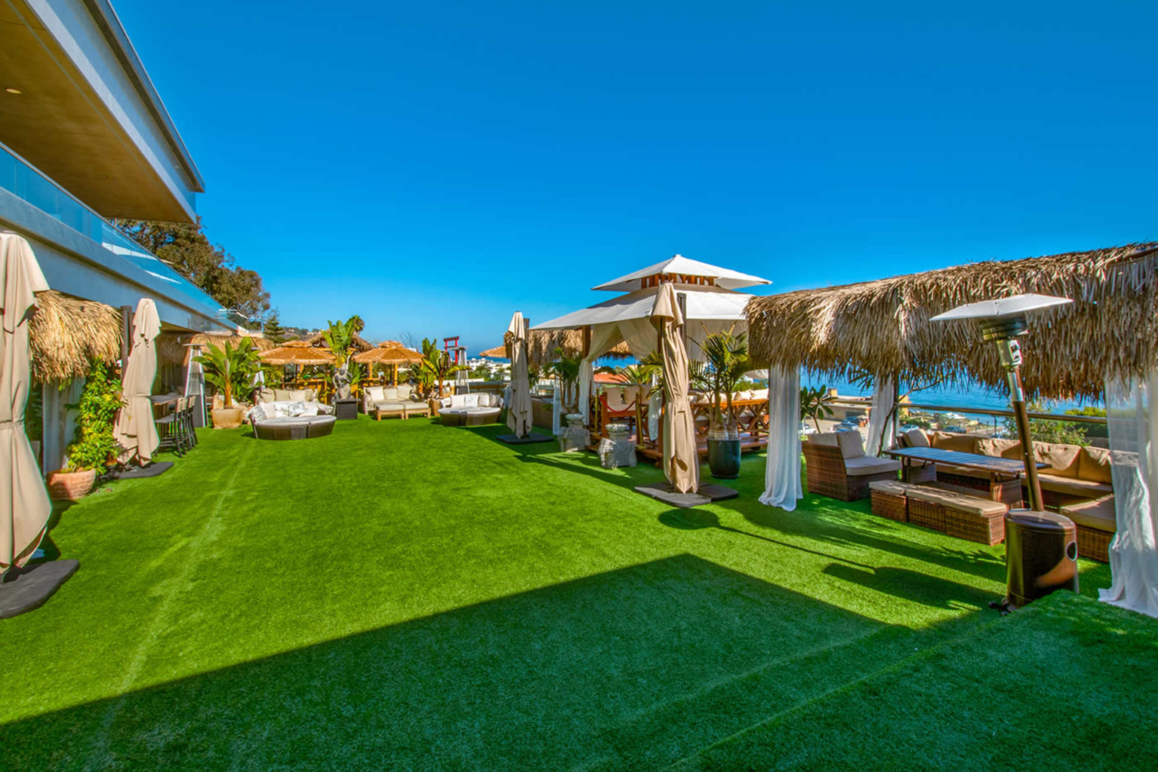 A landscaped outdoor area featuring grass, thatched cabanas, and seating arranged near the ocean.