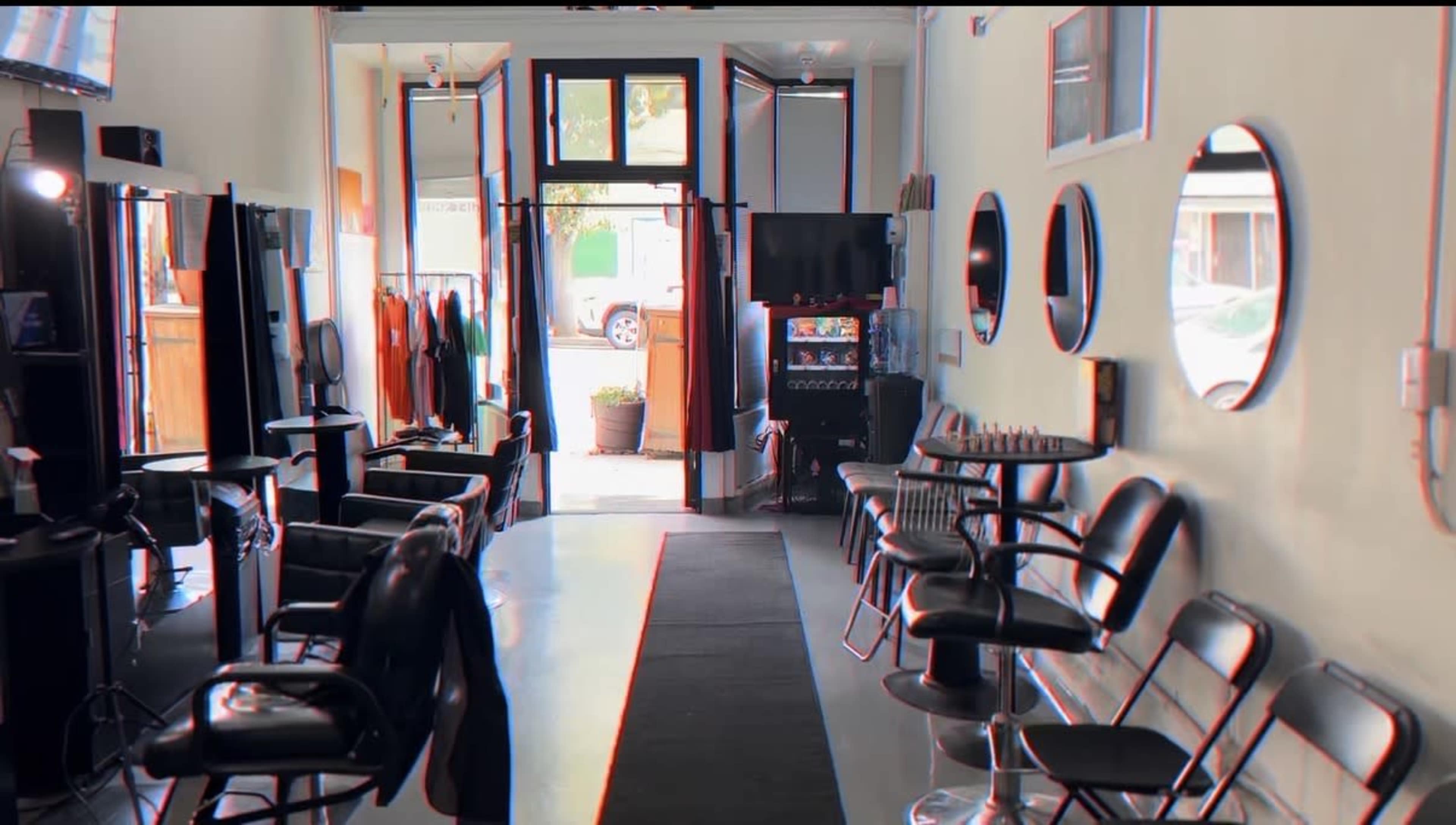 The image shows the interior of a hair salon featuring black chairs, mirrors on the walls, and a view of the entrance with colorful clothing displayed.