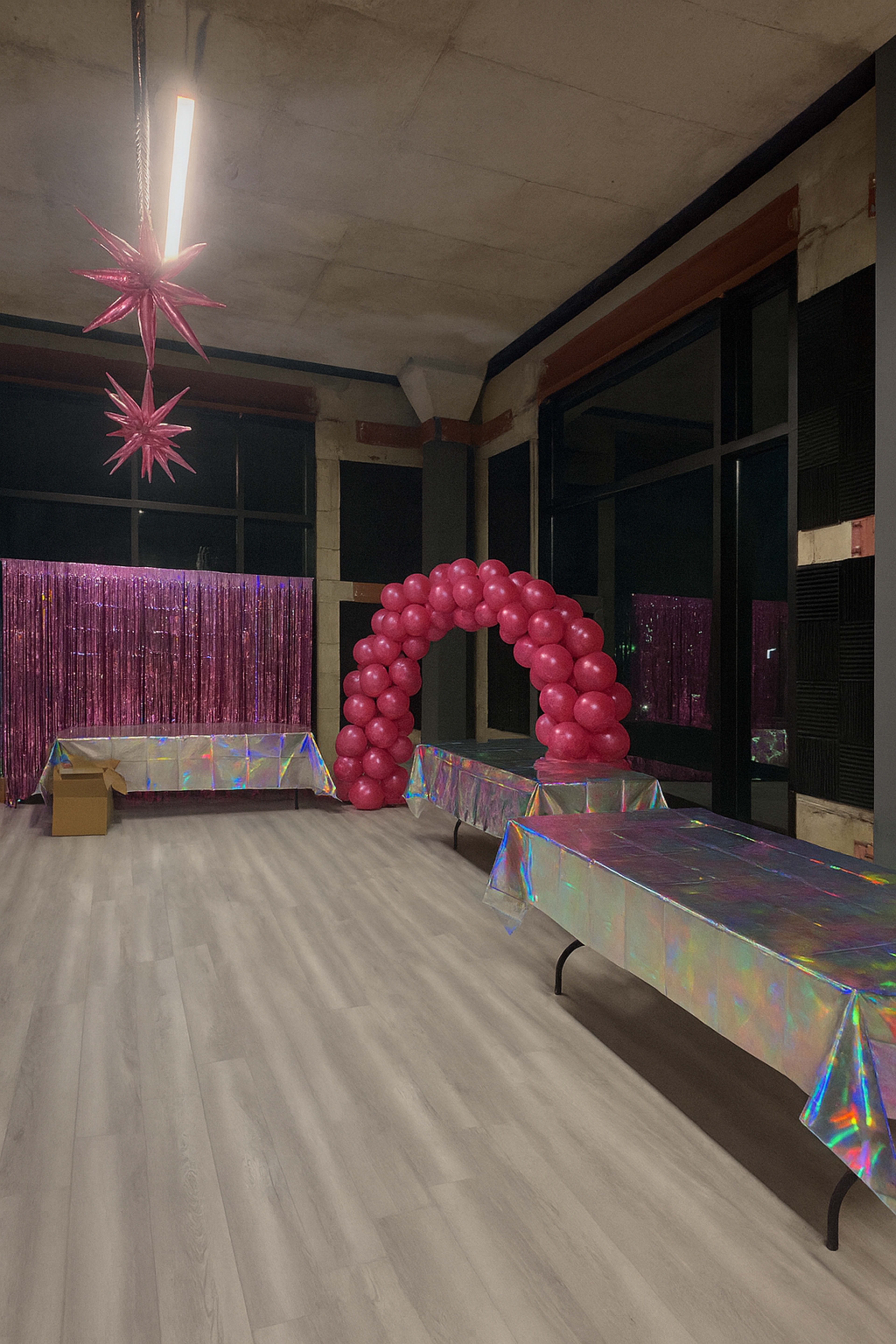 The image shows a party venue with iridescent tables, a pink balloon arch, and a shiny backdrop adorned with fringe.