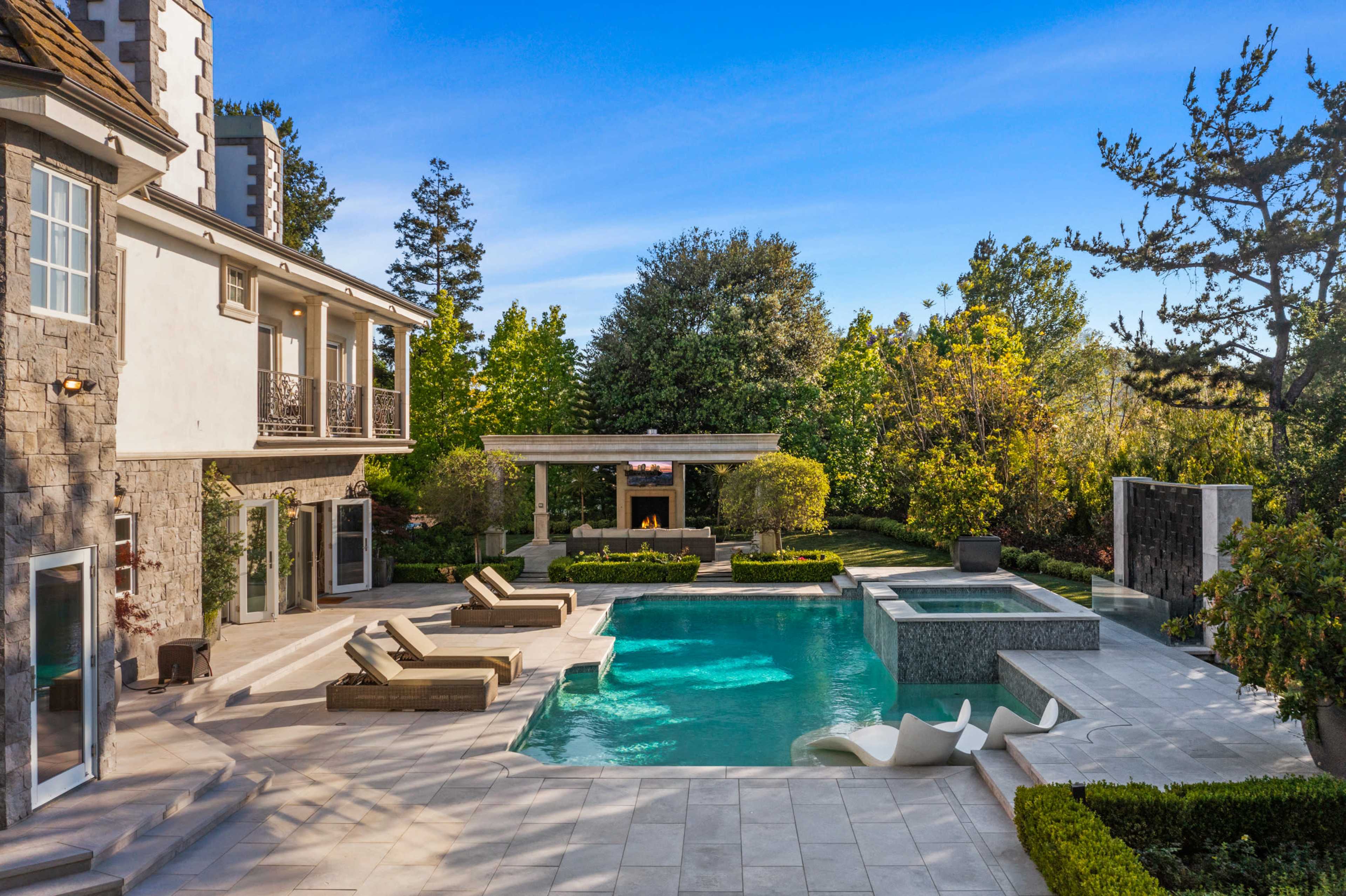 A luxurious residential backyard with a swimming pool, spa, outdoor seating area, and well-manicured landscaping.