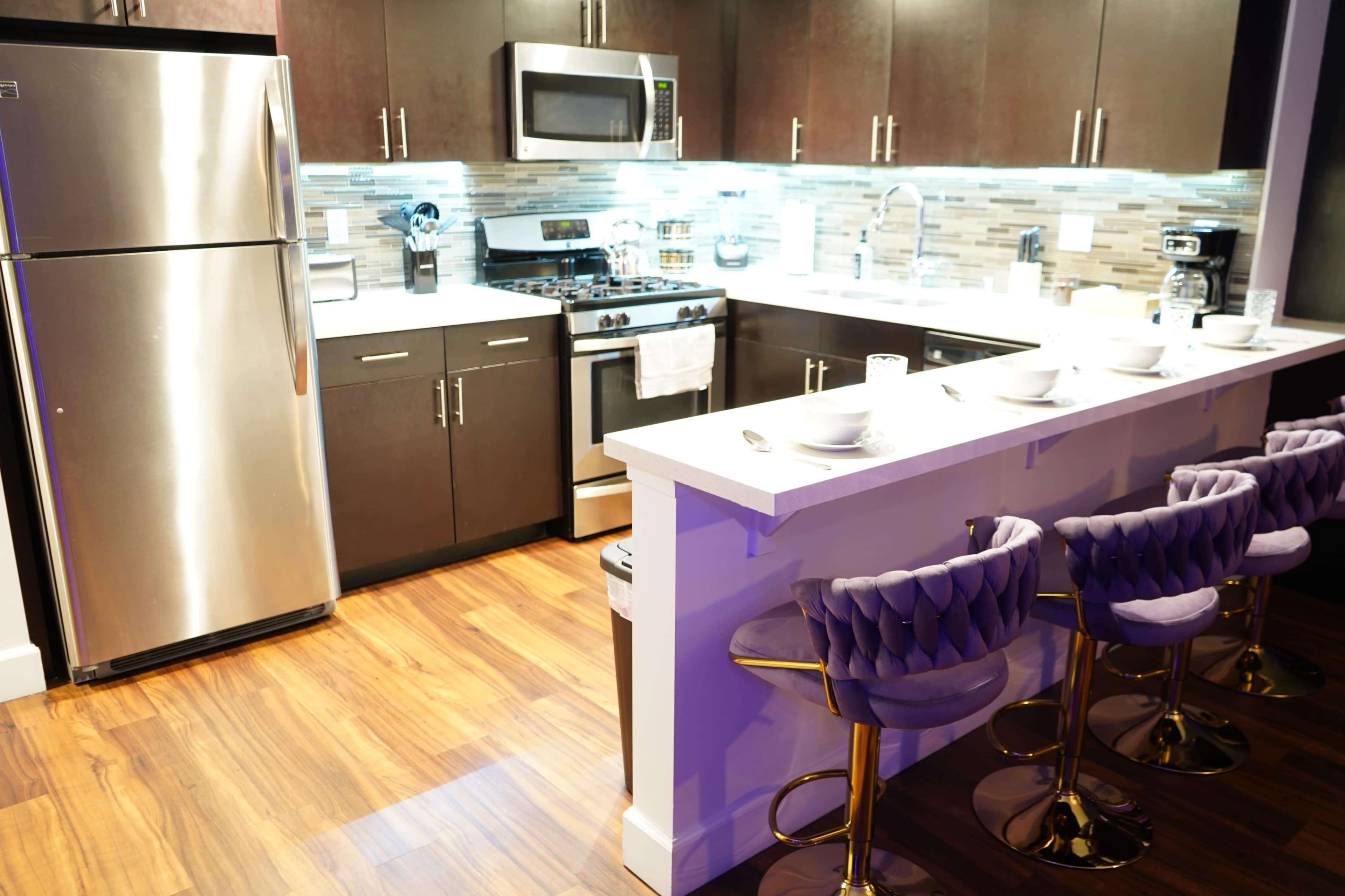 The kitchen features dark cabinetry, a stainless steel refrigerator, a gas stove, and a sleek island with high-backed bar stools.