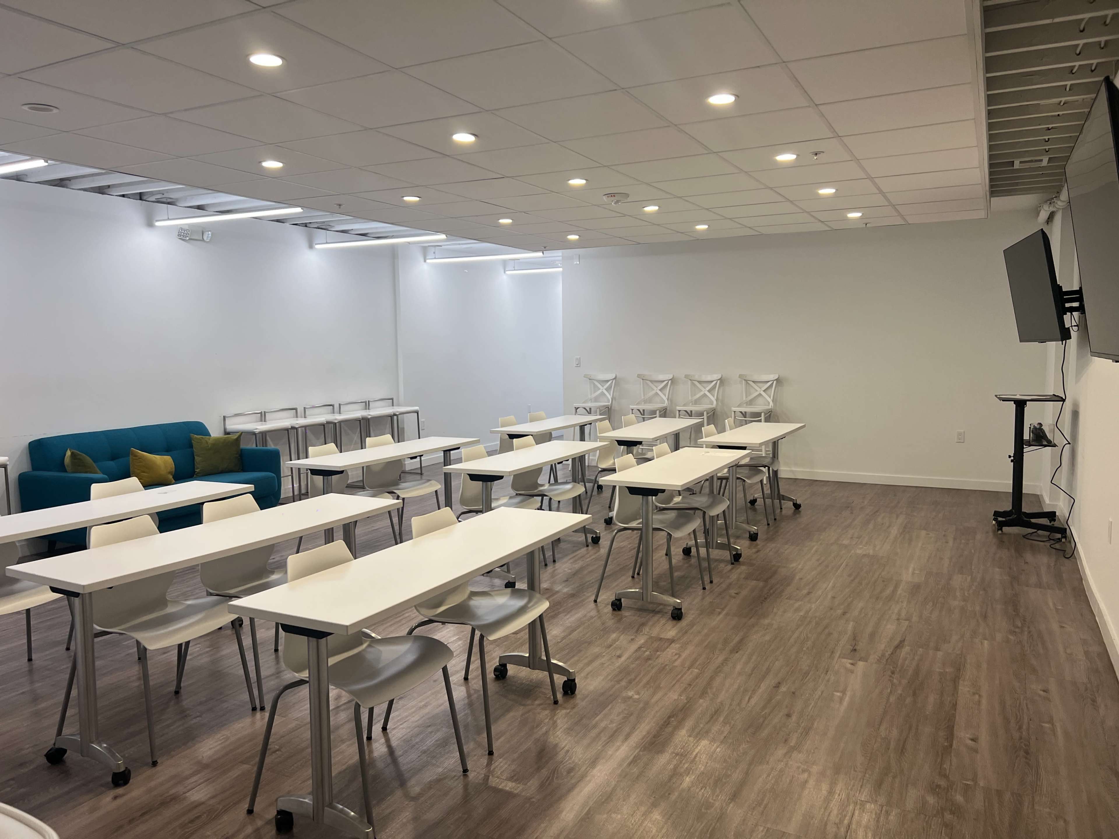 A bright, modern classroom equipped with white tables and chairs arranged in a professional setting.