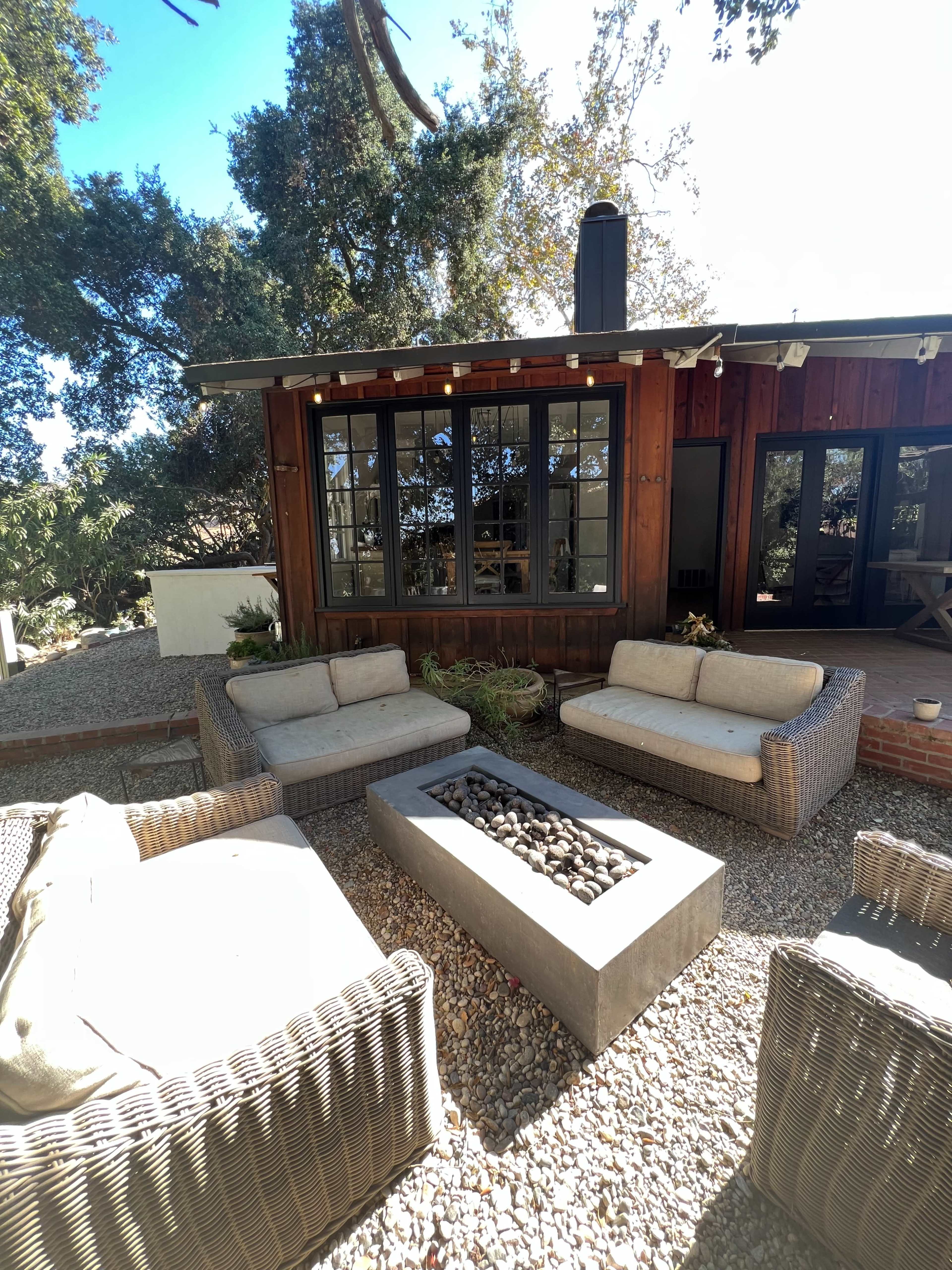 A cozy outdoor seating area features four wicker chairs and a concrete fire pit surrounded by a gravel surface.