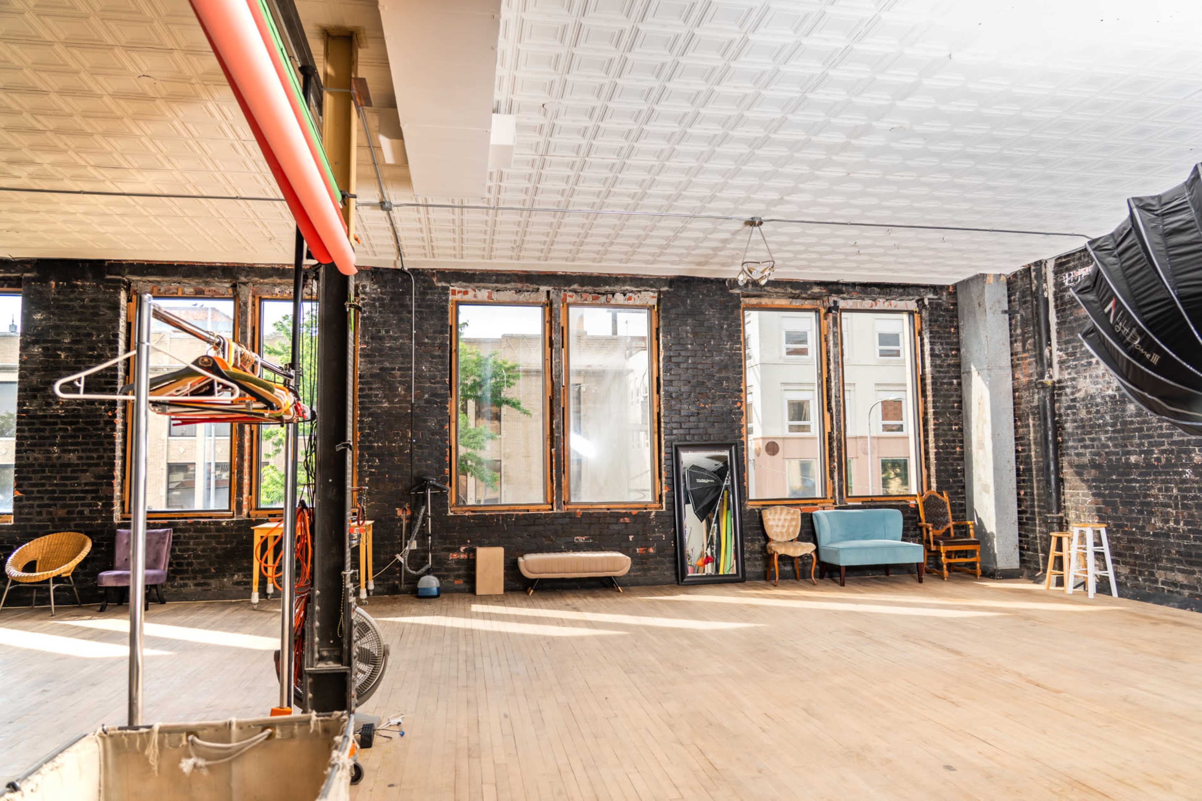 A spacious, brightly lit studio features exposed brick walls, large windows, and a variety of seating options.