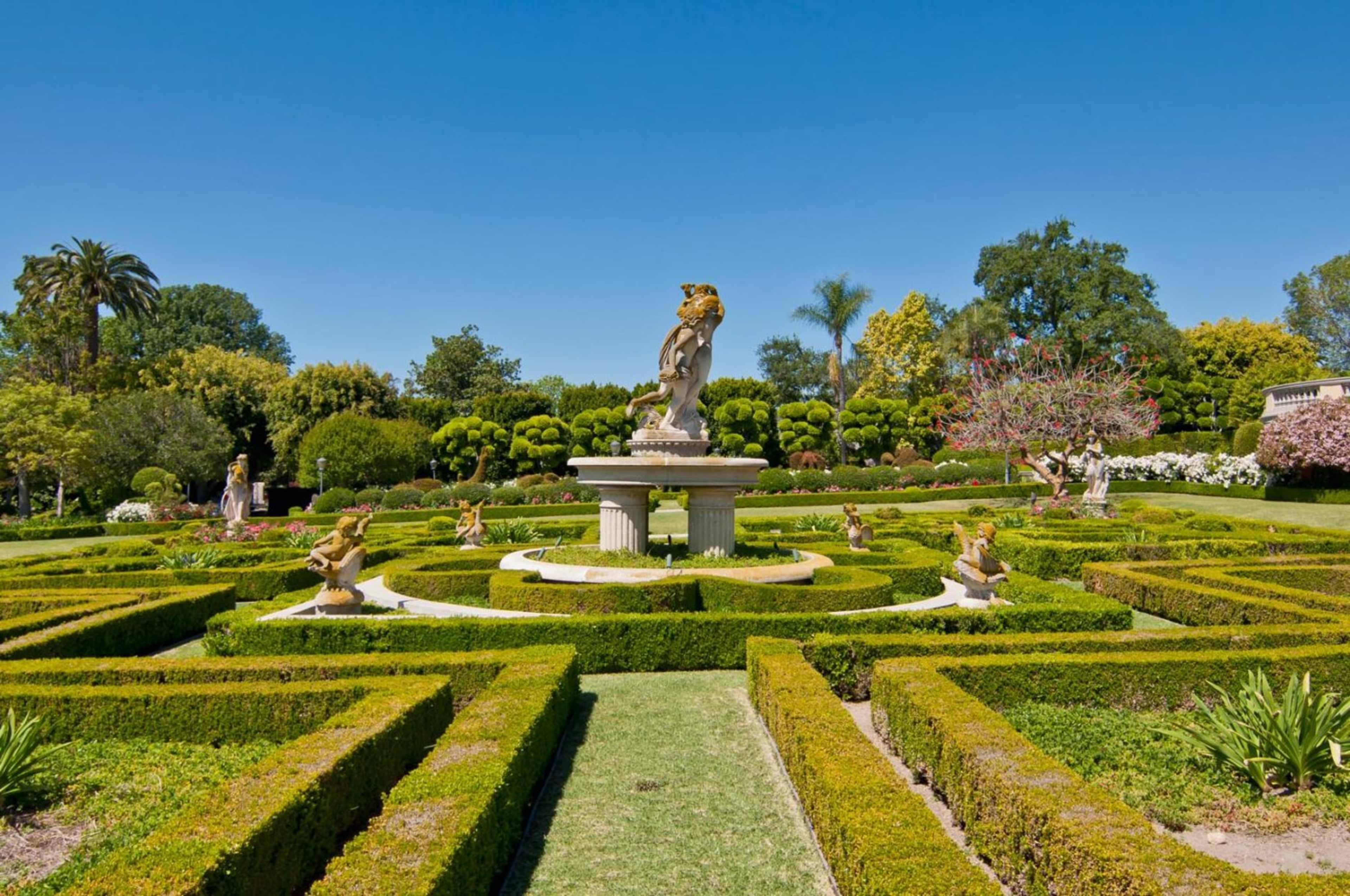 A well-maintained garden featuring a central fountain with a statue, surrounded by neatly trimmed hedges and landscaped flower beds.