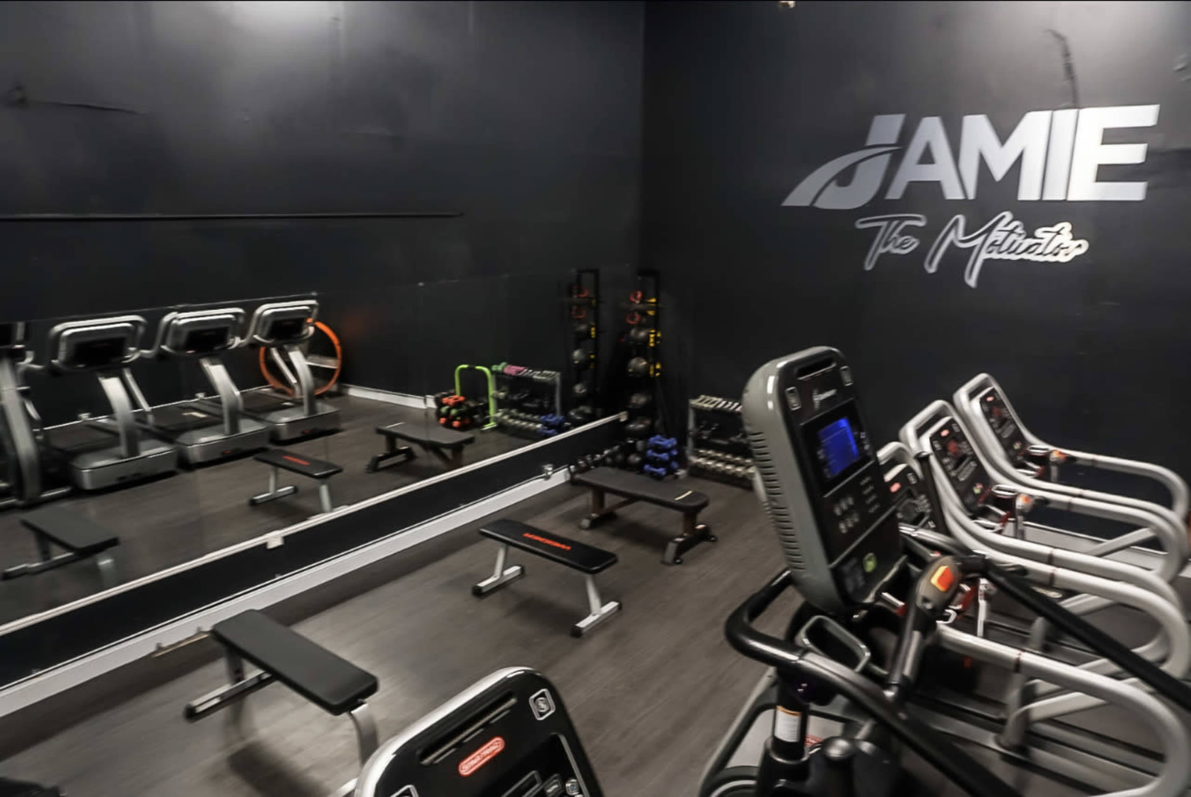 A small gym with exercise equipment, including benches, weights, and cardio machines, against a black wall.