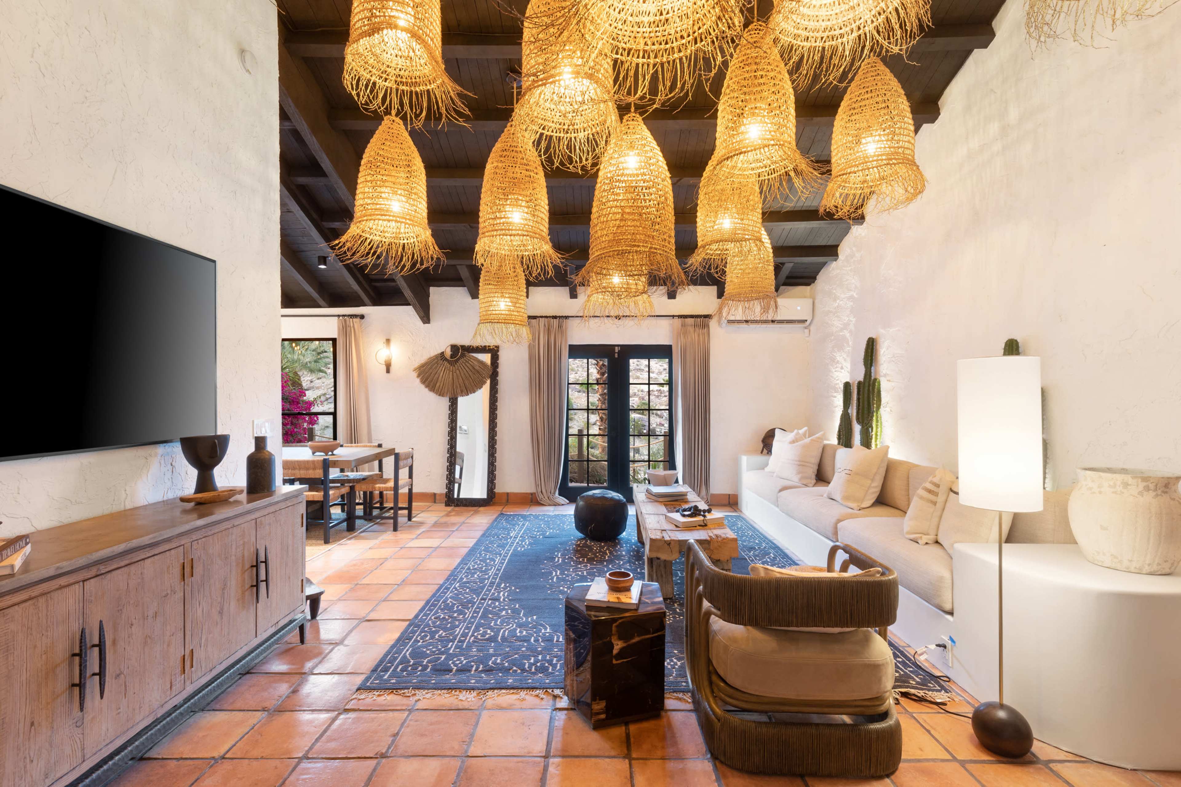 A living room features a sofa, textured decor, a large television, a dining area, and several pendant lights hanging from the ceiling.