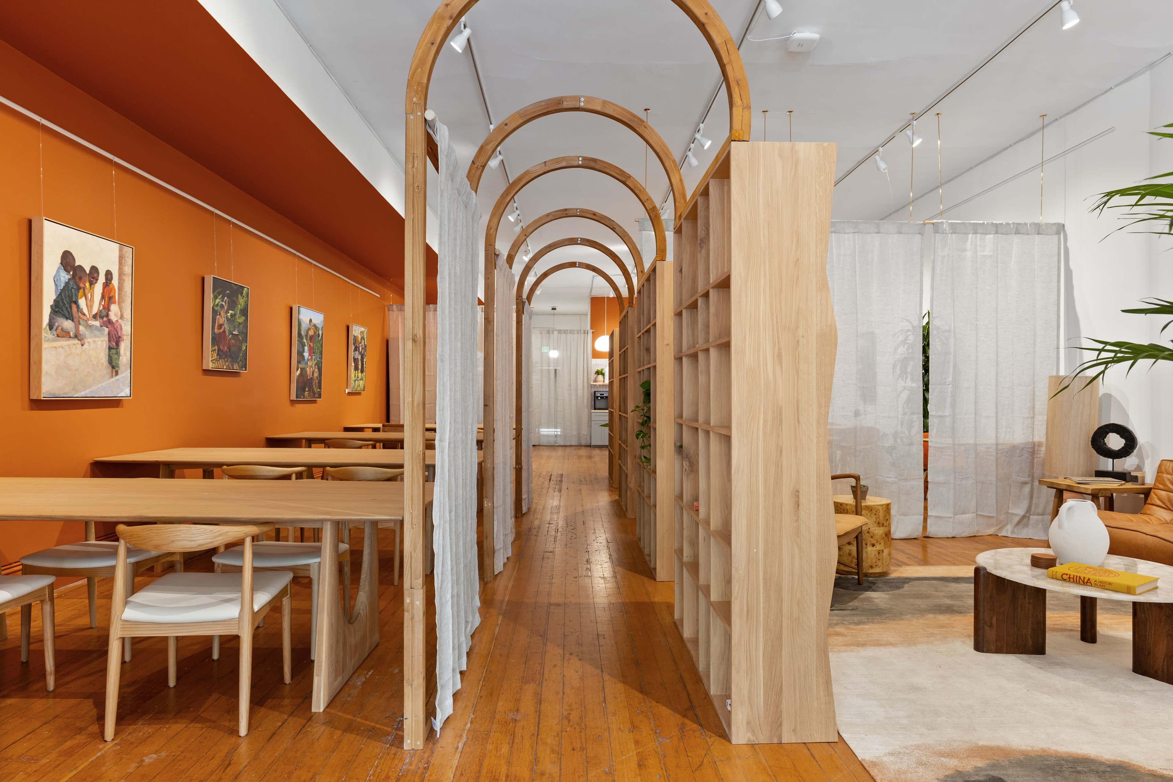 A modern interior space with wooden arches dividing a dining area and shelves, accompanied by orange walls and artwork.