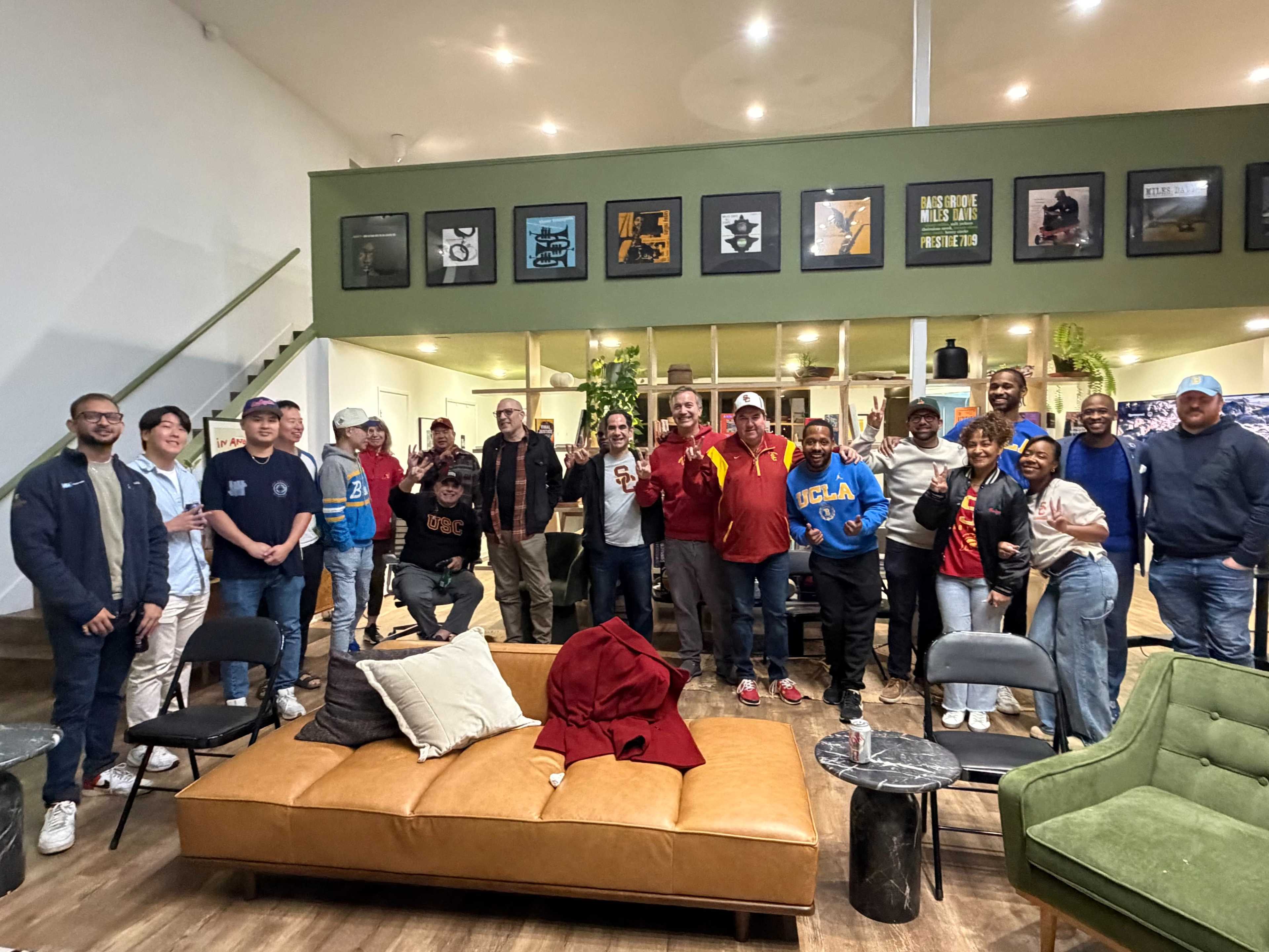 A large group of people stands together in a brightly lit room with modern furniture and framed artwork on the walls.