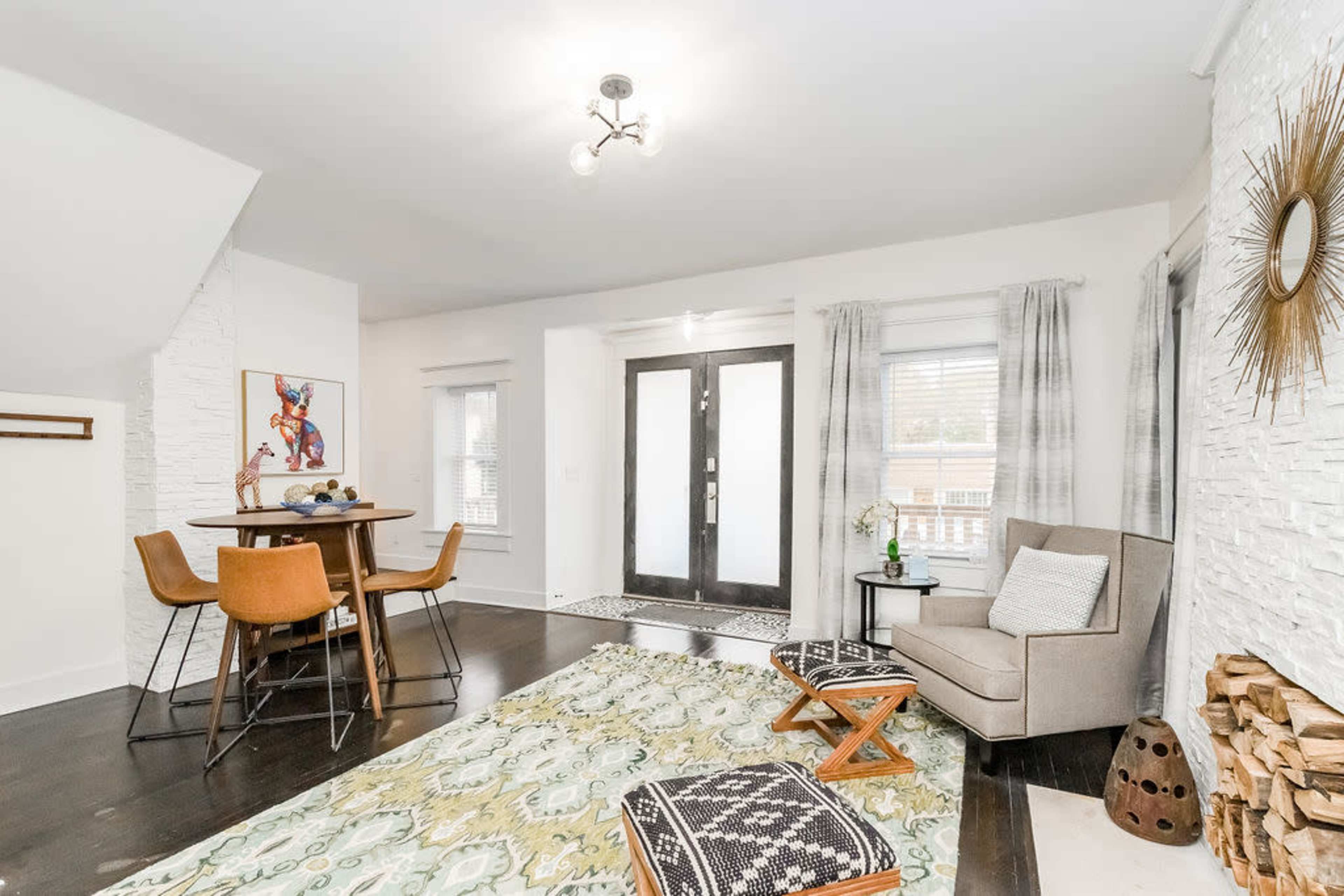 A bright living room with a round dining table, a seating area featuring an armchair, and decorative elements on the walls.