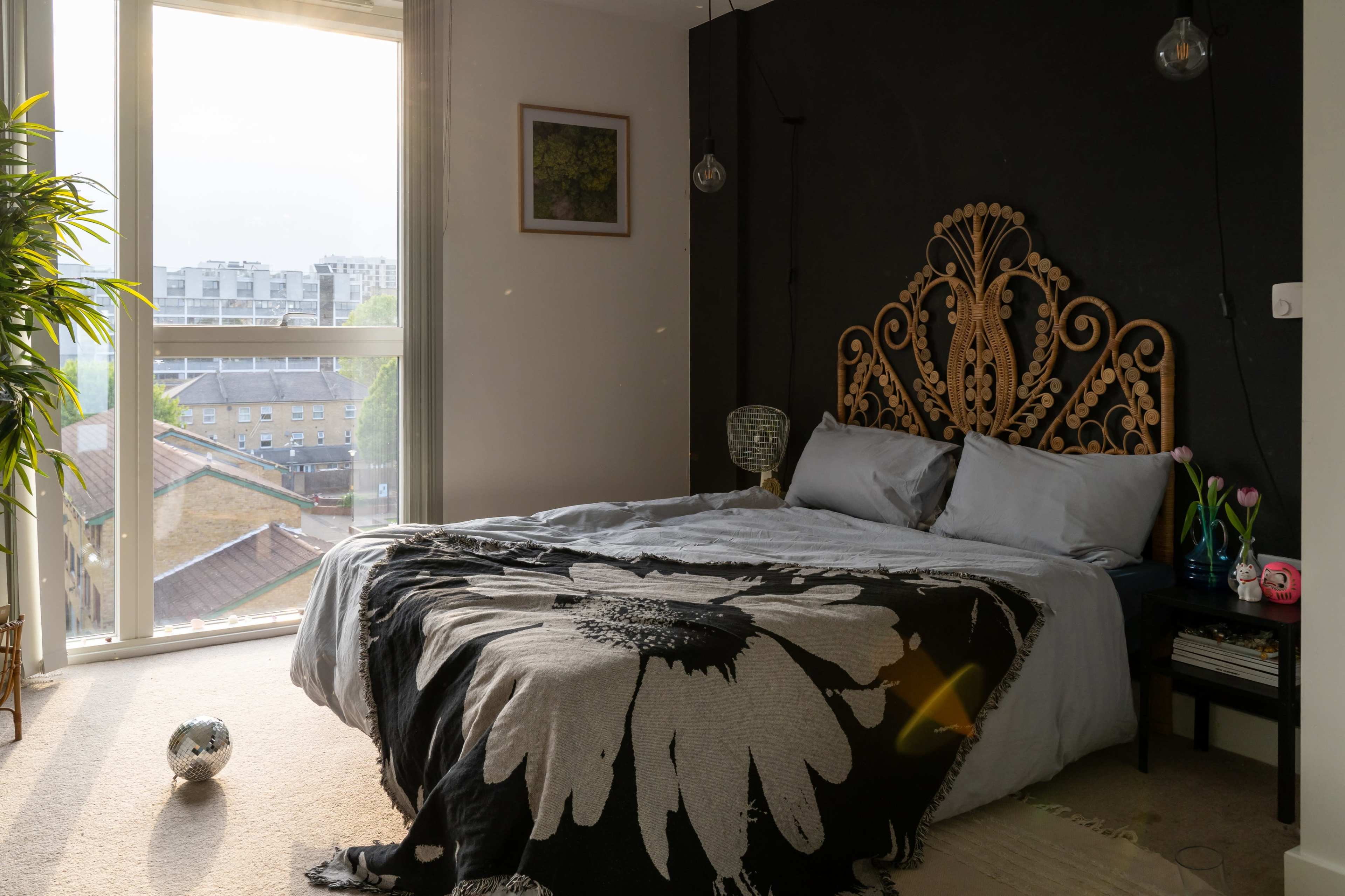 A neatly made bed with a decorative headboard is positioned against a wall, while large windows allow natural light to fill the room.