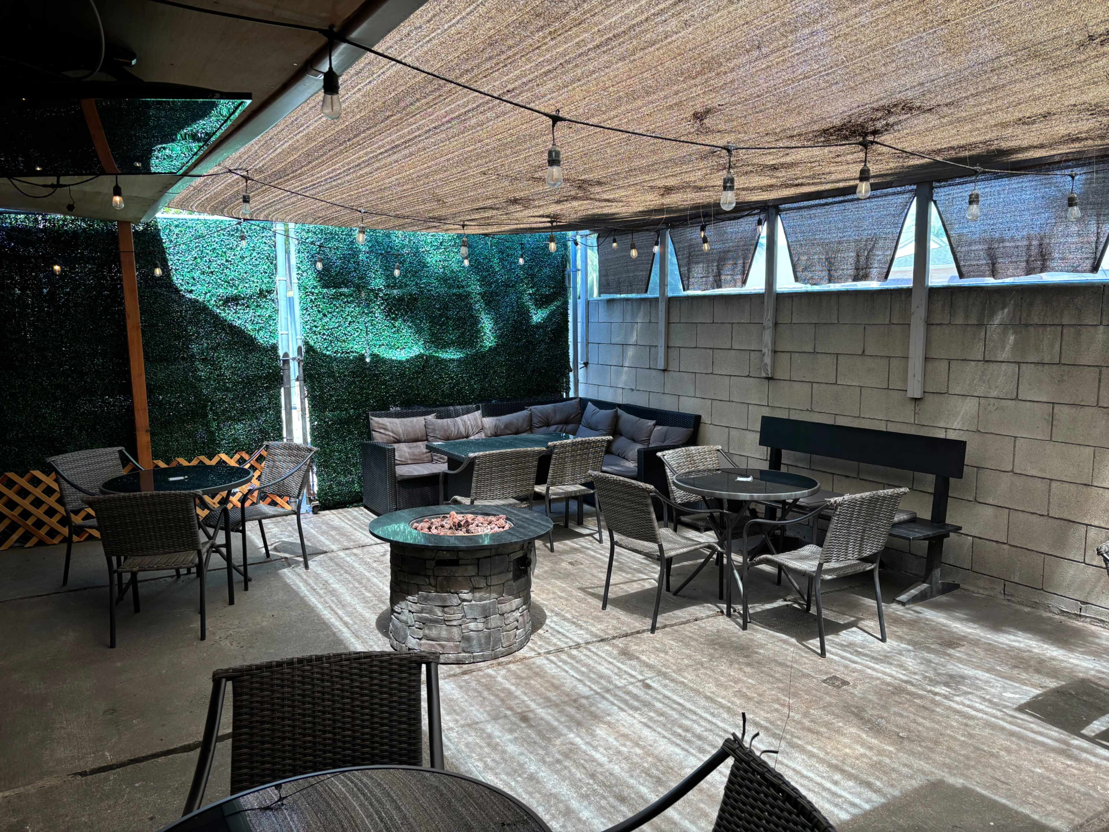 A shaded outdoor seating area features a circular fire pit surrounded by tables and chairs, with a large sectional couch against the wall.