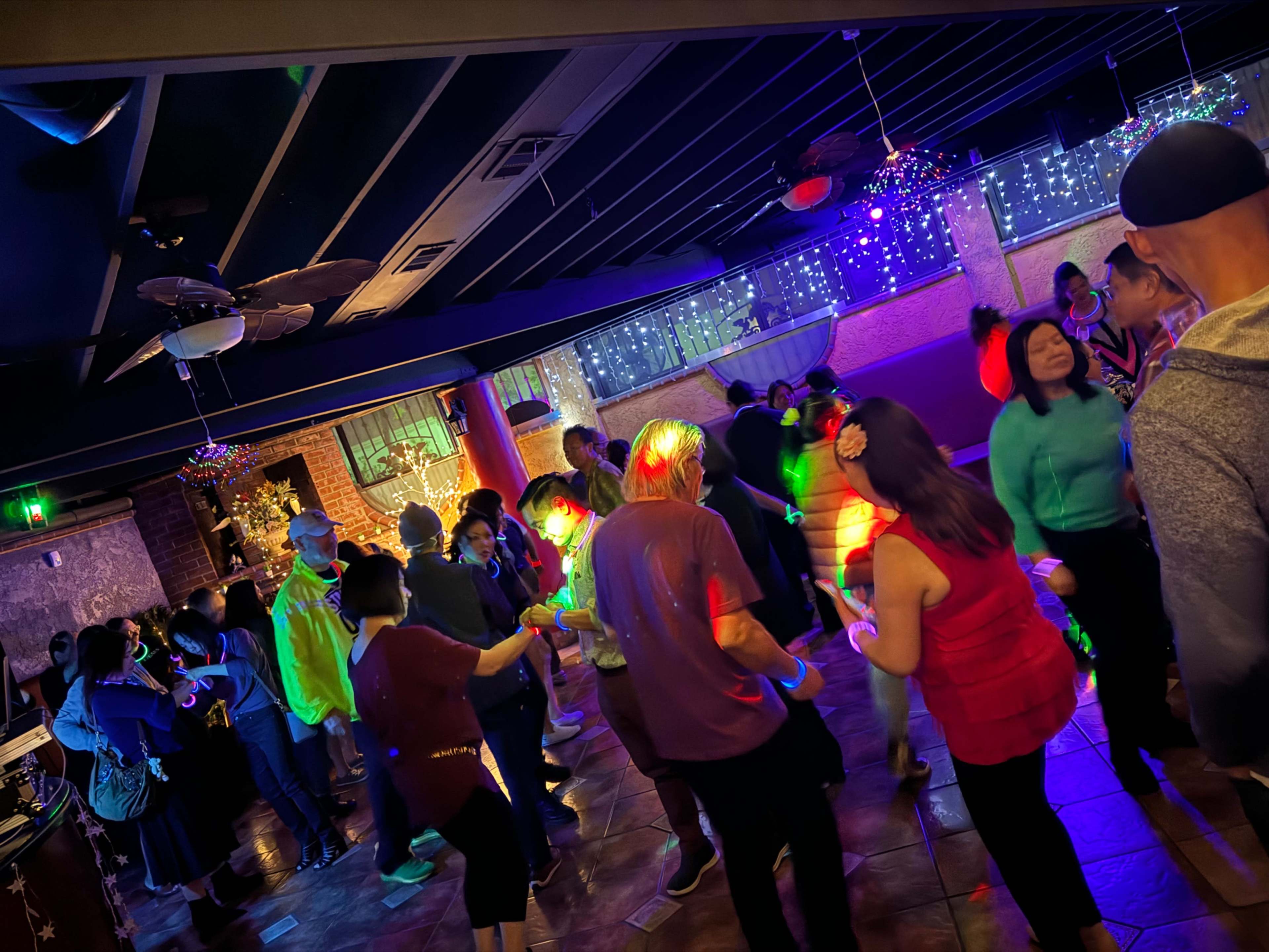 A lively crowd dances in a dimly lit venue adorned with colorful lights and festive decorations.