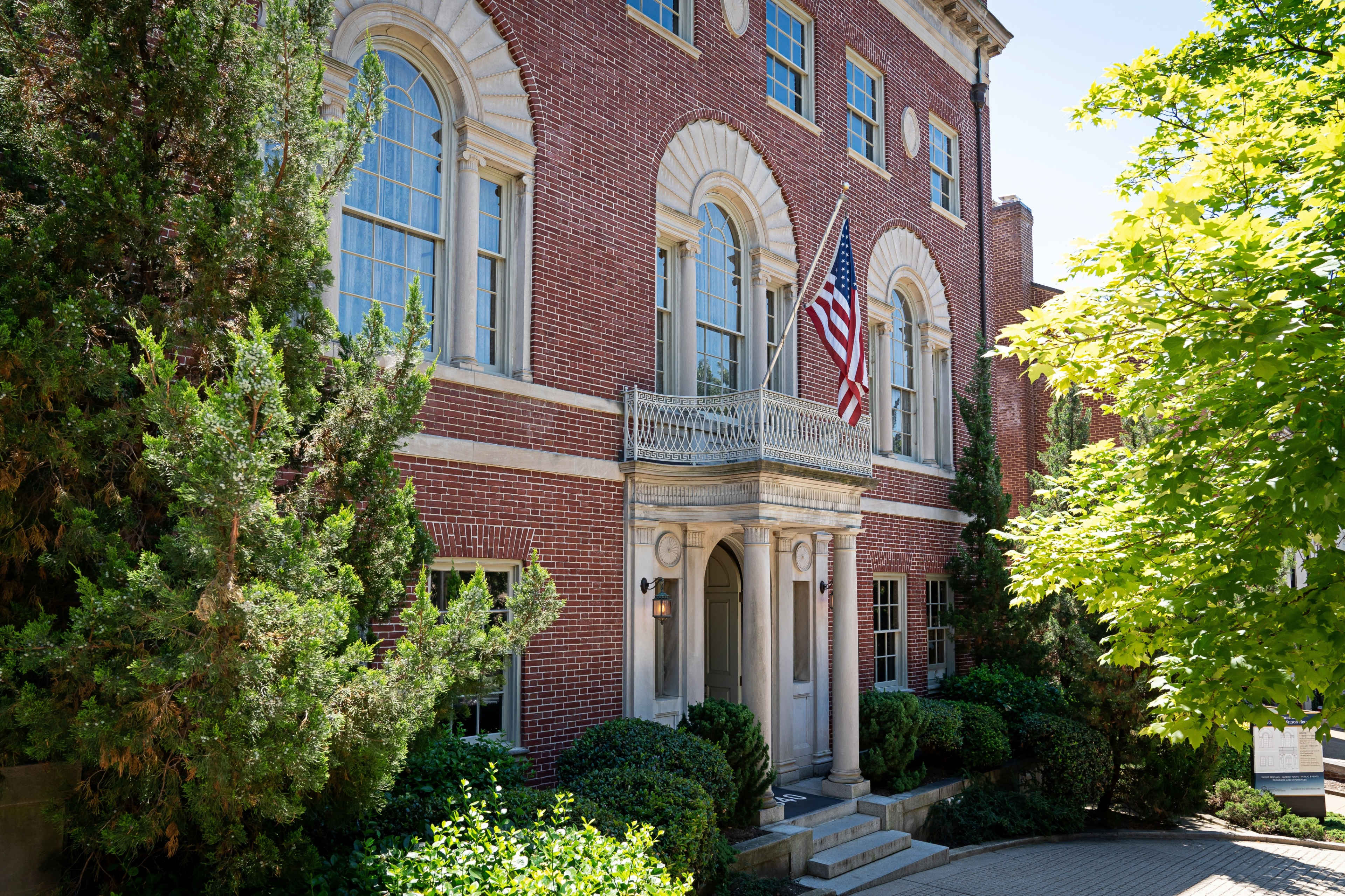 A brick building with large windows and a decorative entrance displays an American flag on a balcony.