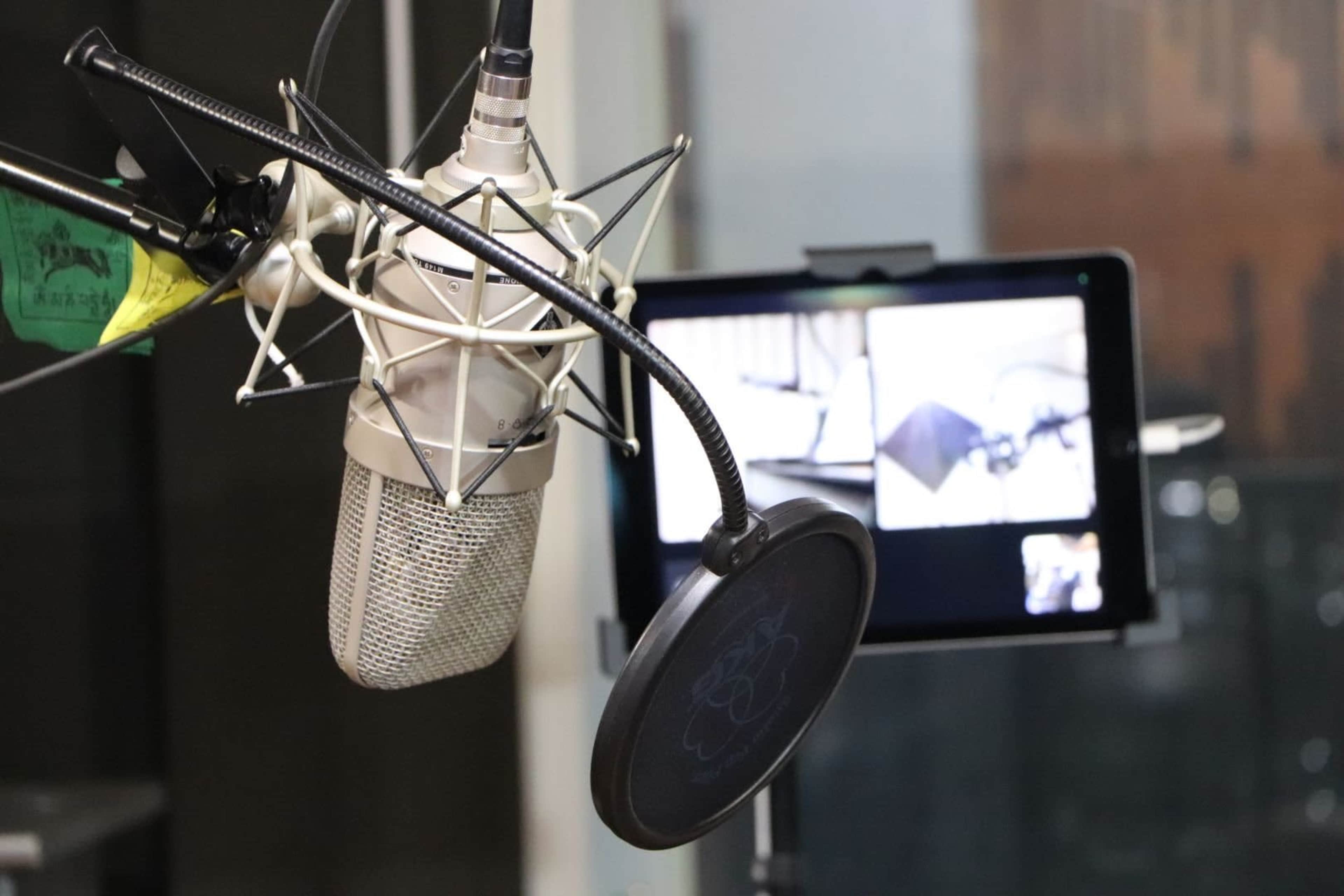 A studio microphone is positioned in front of a tablet displaying a video call.