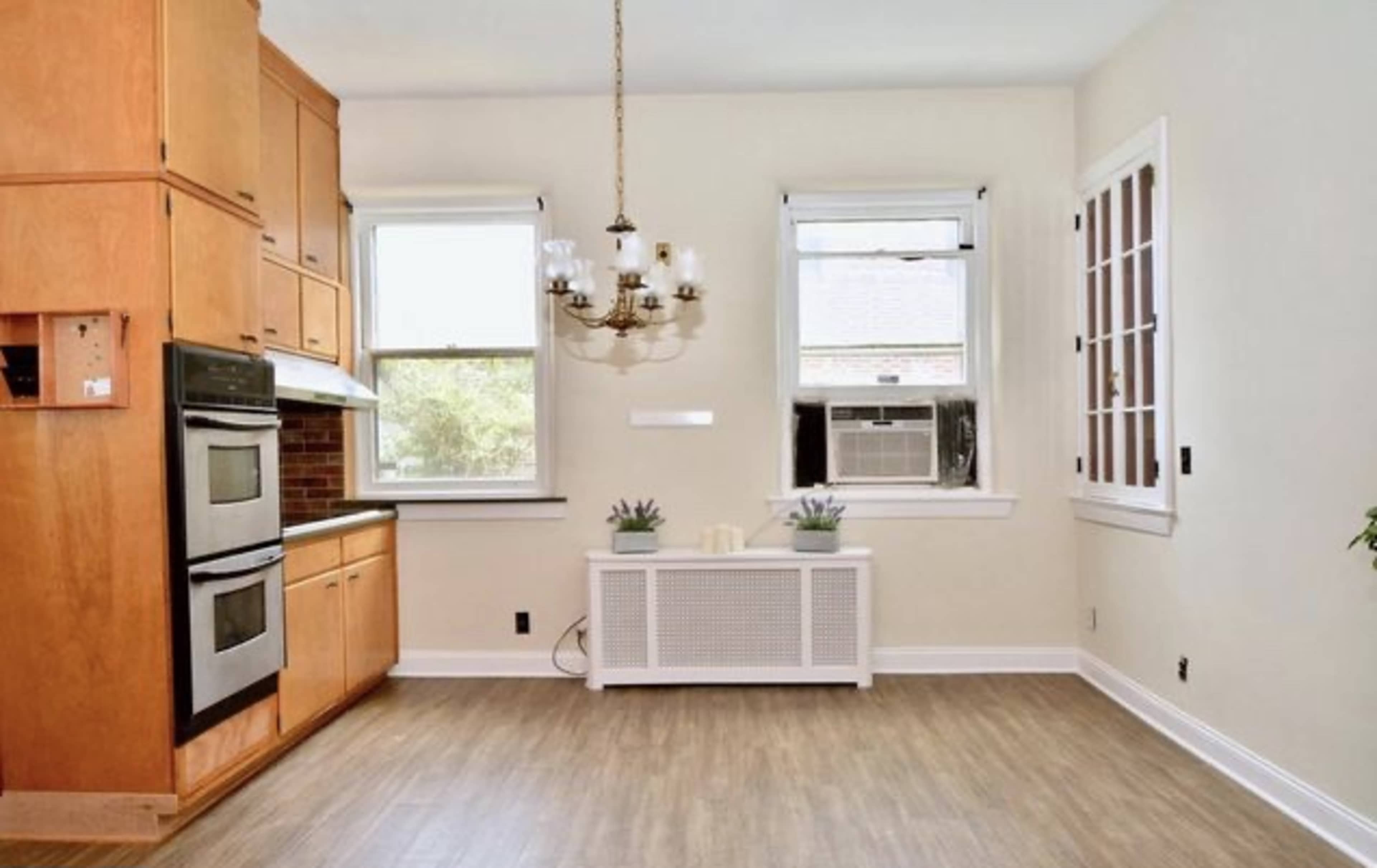 A kitchen area featuring wooden cabinetry, stainless steel appliances, two windows, and a central chandelier.