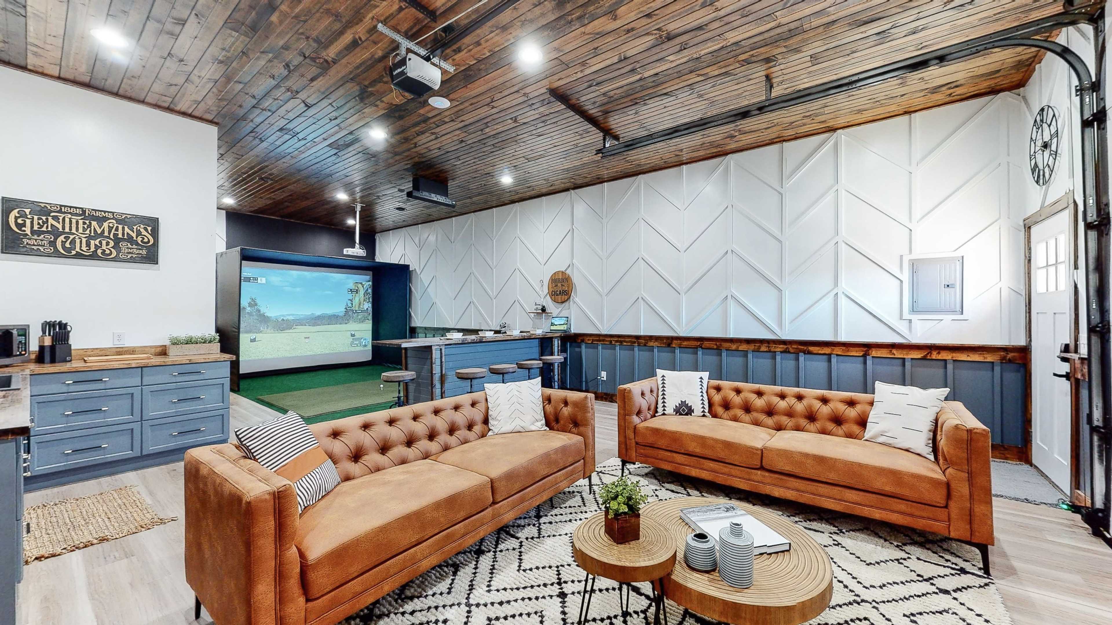 A cozy lounge area with tan couches, a decorative rug, and a golf simulator in the background.