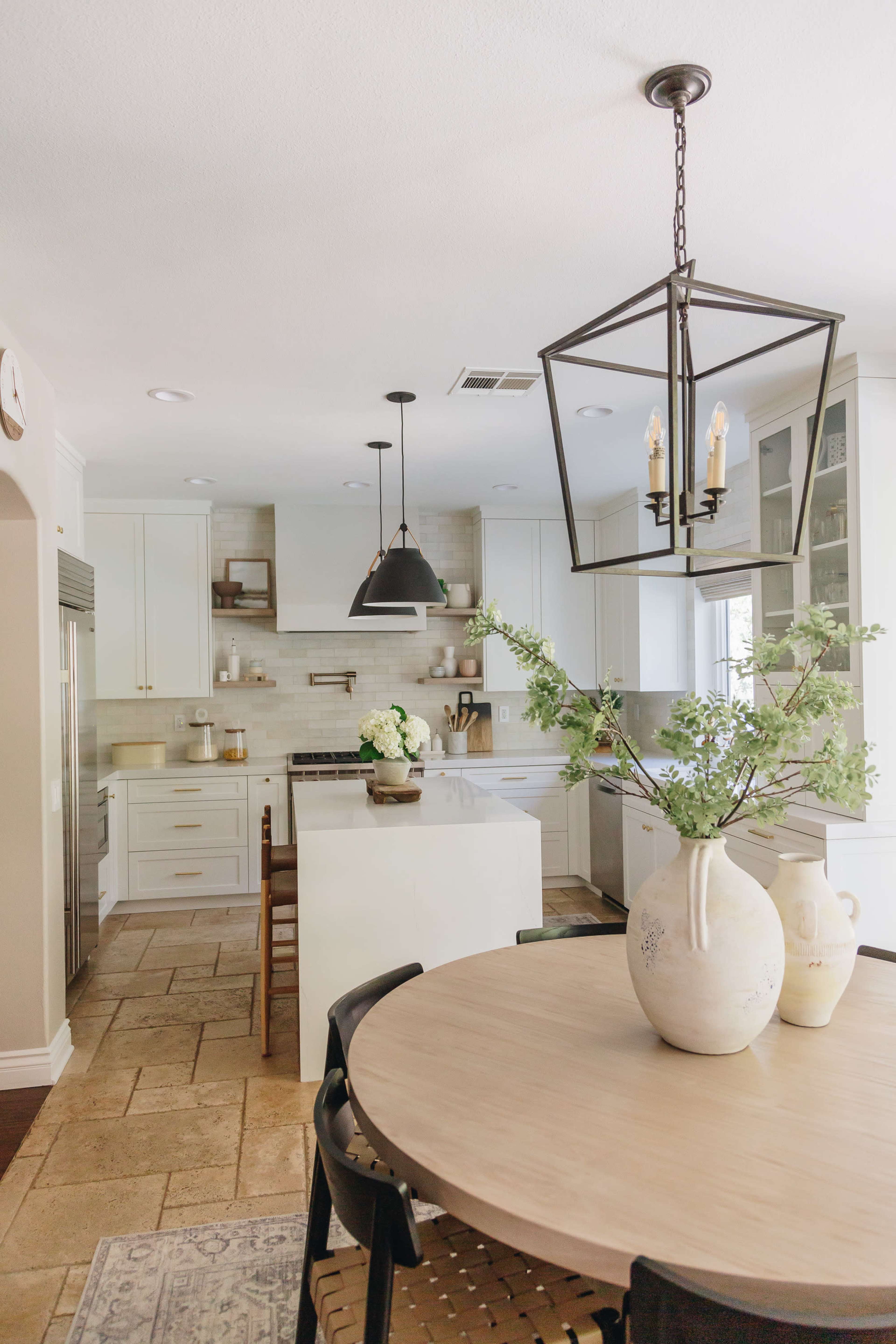 A bright, modern kitchen features white cabinetry, a large island, and a dining table surrounded by black chairs.