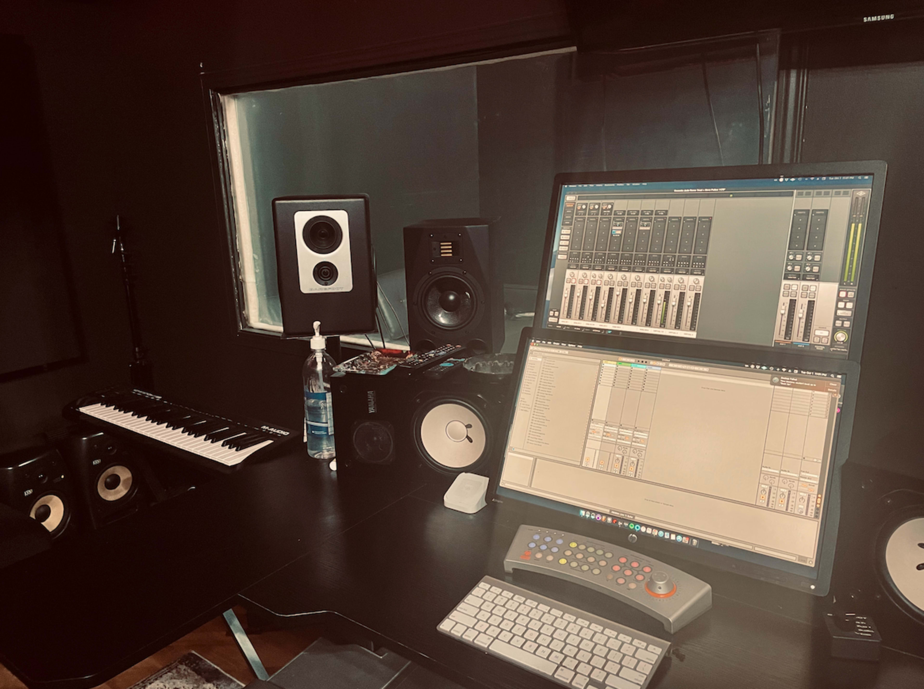 The image shows a music production studio workspace with a computer monitor, audio interface, speakers, MIDI keyboard, and various sound equipment.