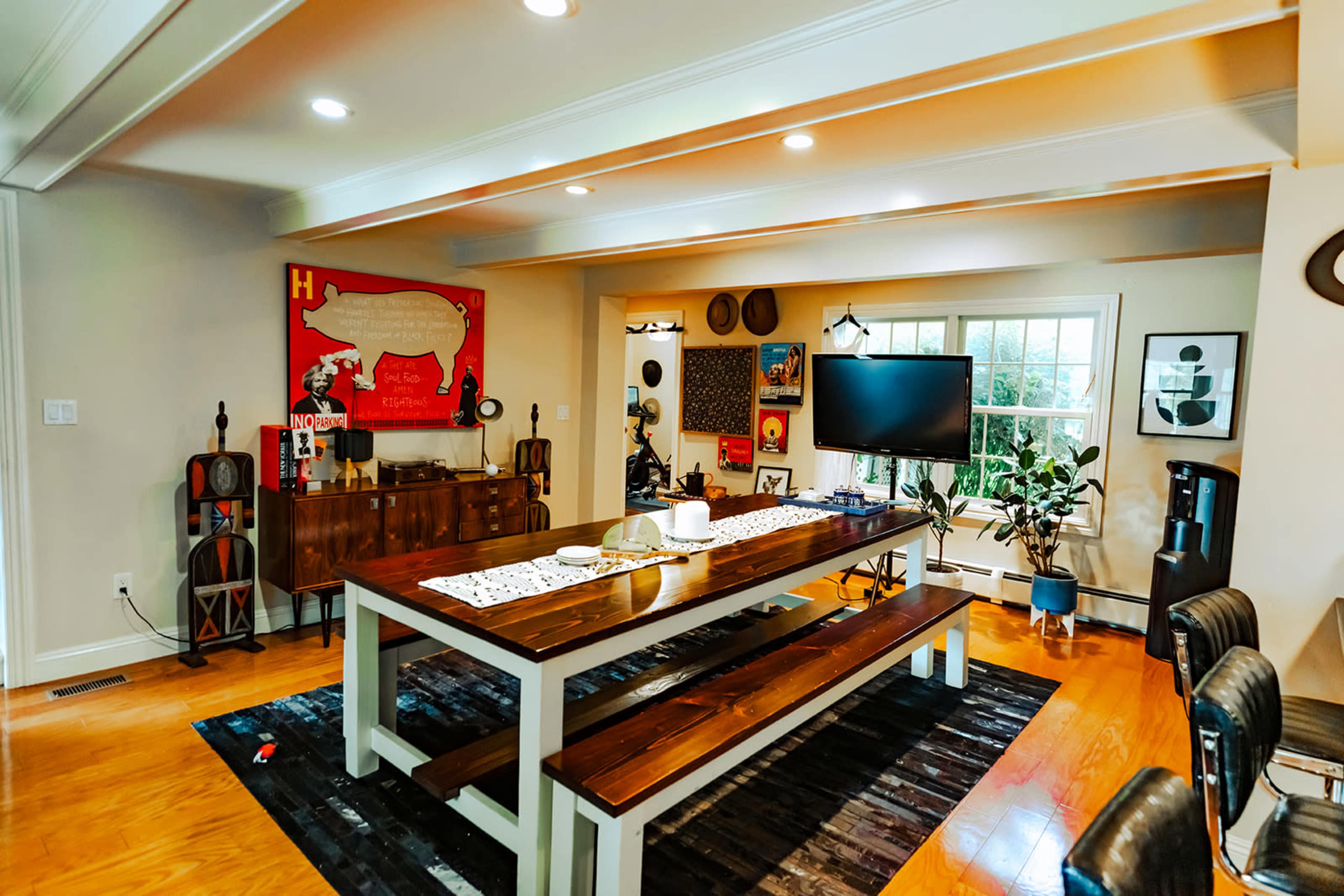 A modern dining area with a long wooden table, surrounded by black chairs, and large windows overlooking a garden.