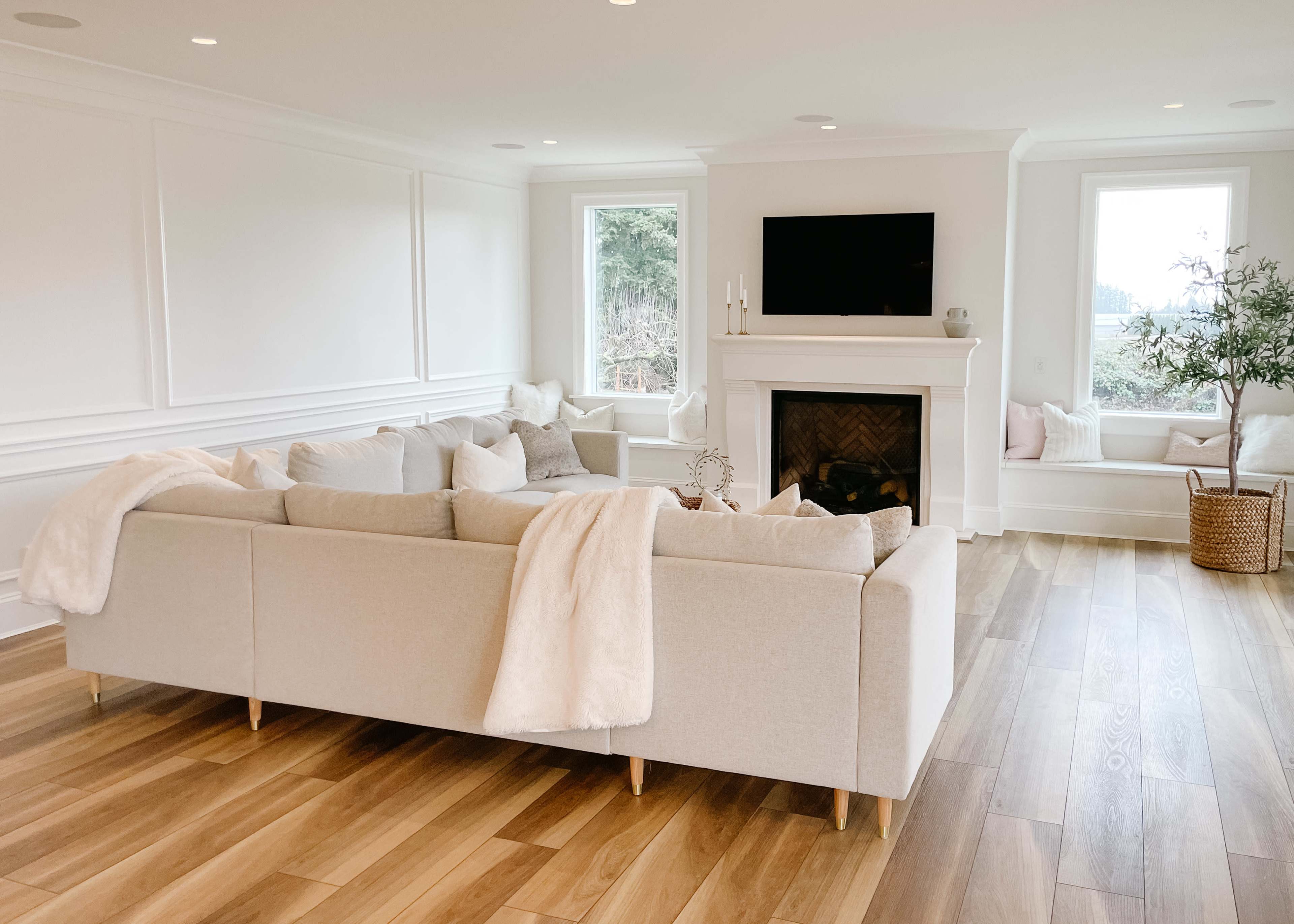 A light-filled living room features a beige sectional sofa, a fireplace, and large windows with a cozy window seat.
