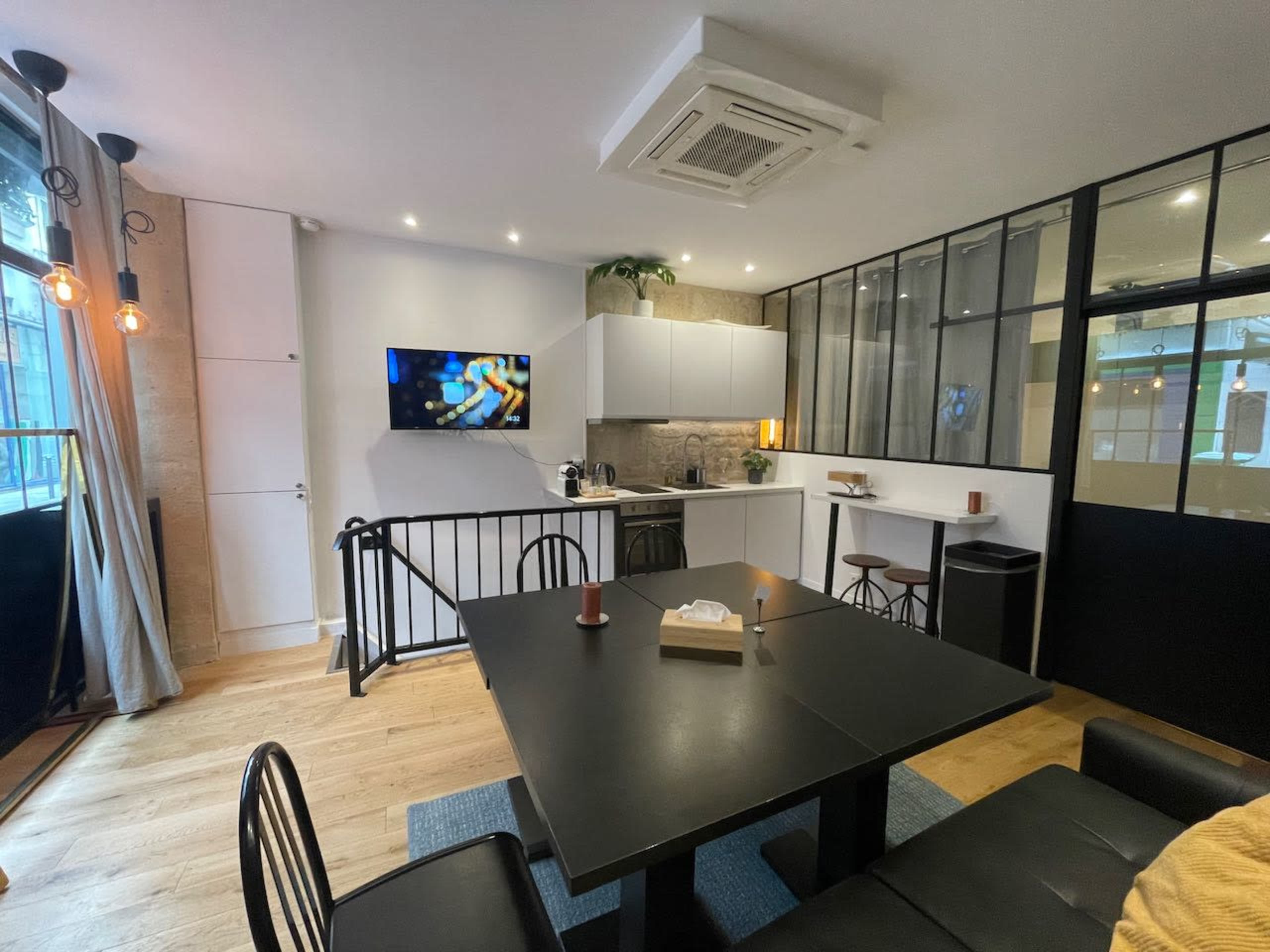 A modern kitchen and dining area features a black table, chairs, and a large window with industrial-style glass partitions.