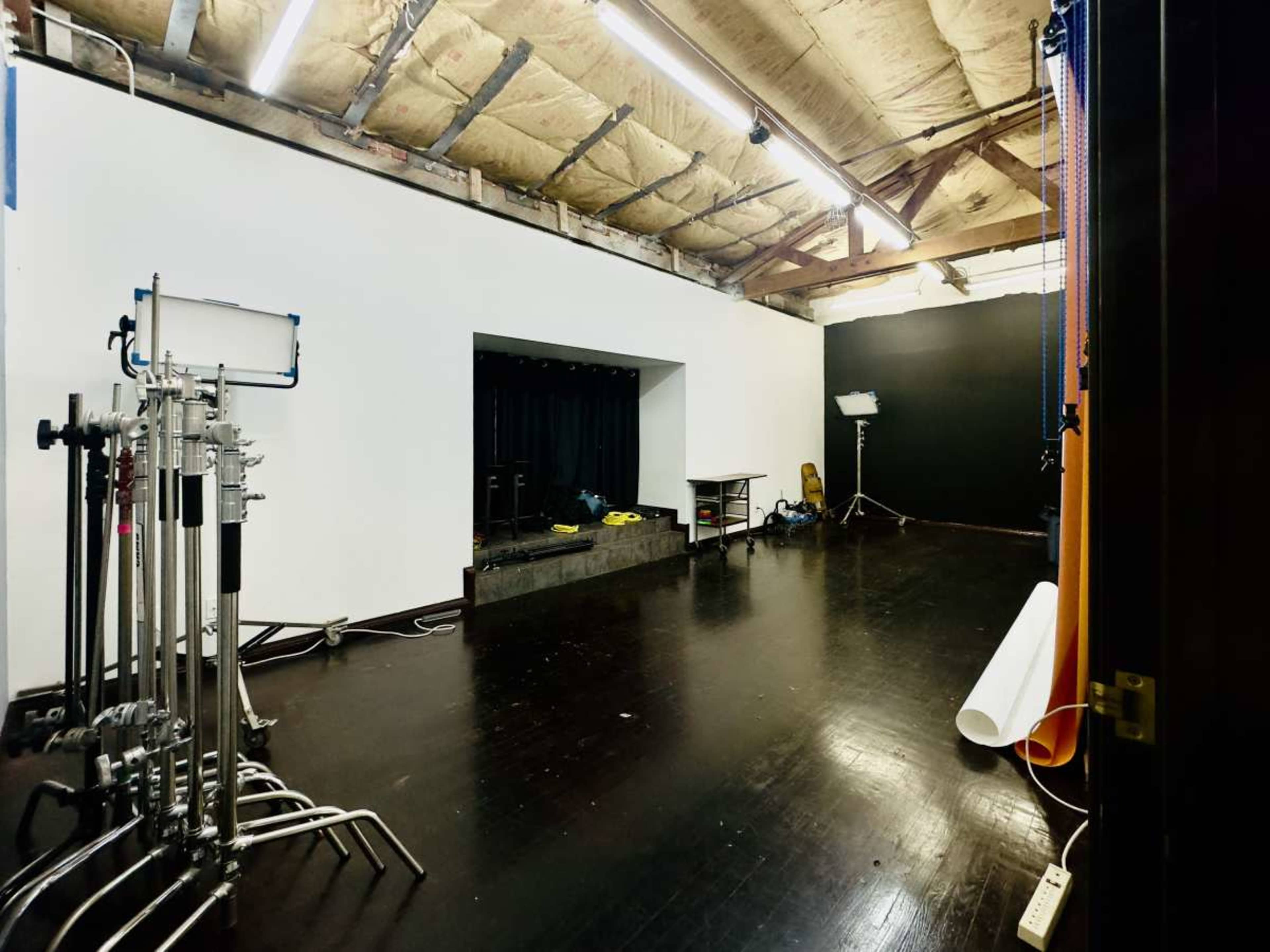 A spacious film studio with a black wall, a white backdrop, and various lighting equipment arranged on the floor.
