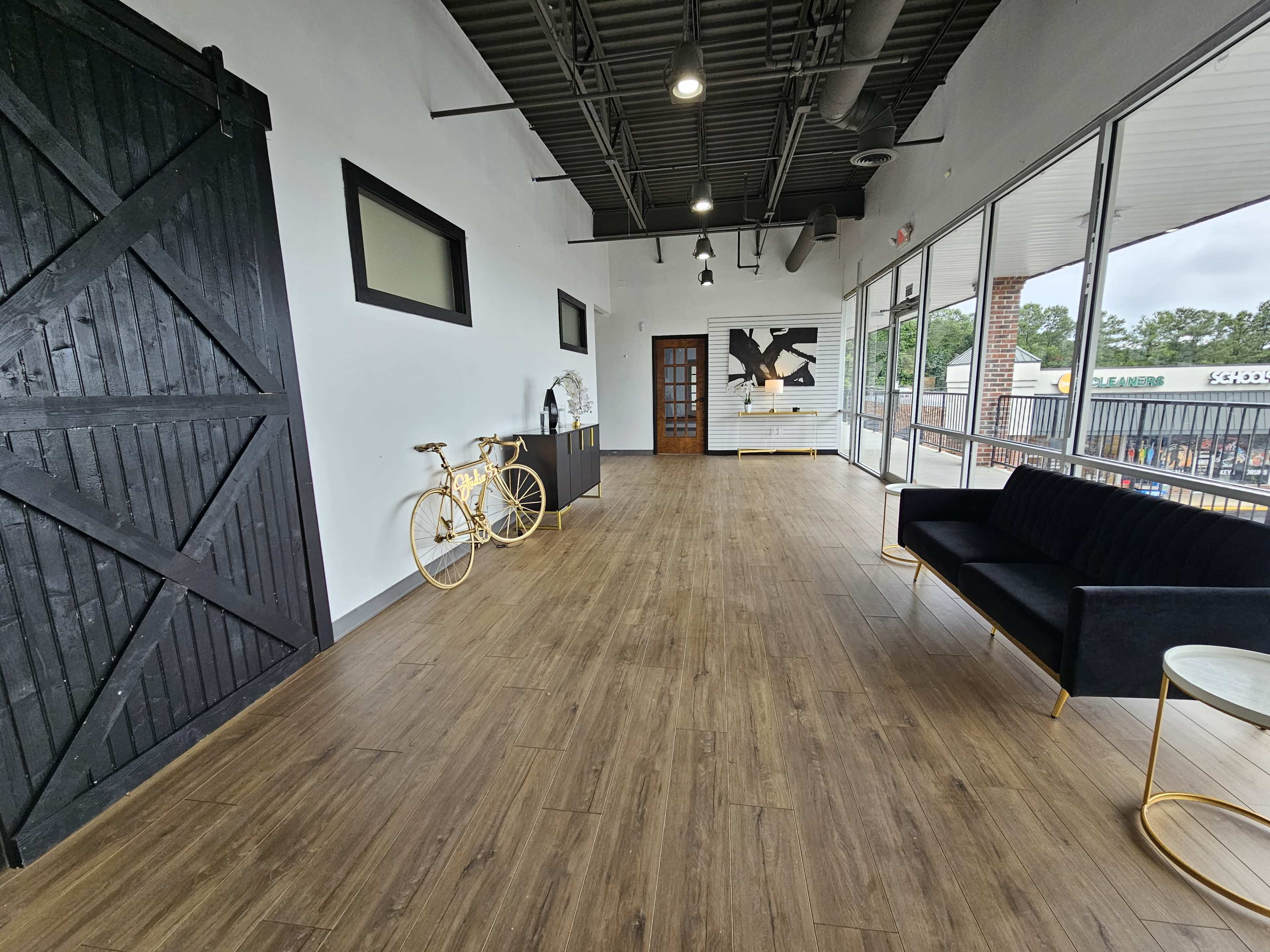 A spacious, modern interior with a wooden floor, two large black doors, a black couch, a small circular table, and a decorative yellow bicycle against the wall.