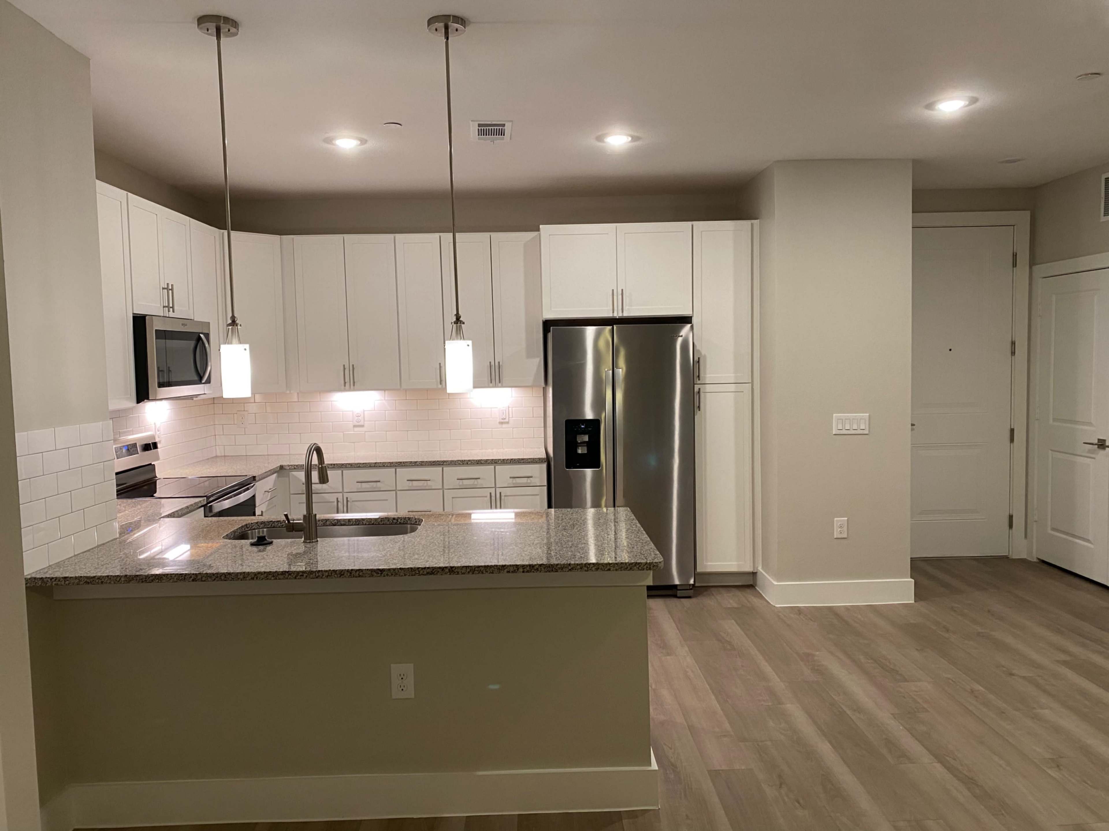 A modern kitchen features white cabinetry, stainless steel appliances, and a granite countertop with pendant lighting.