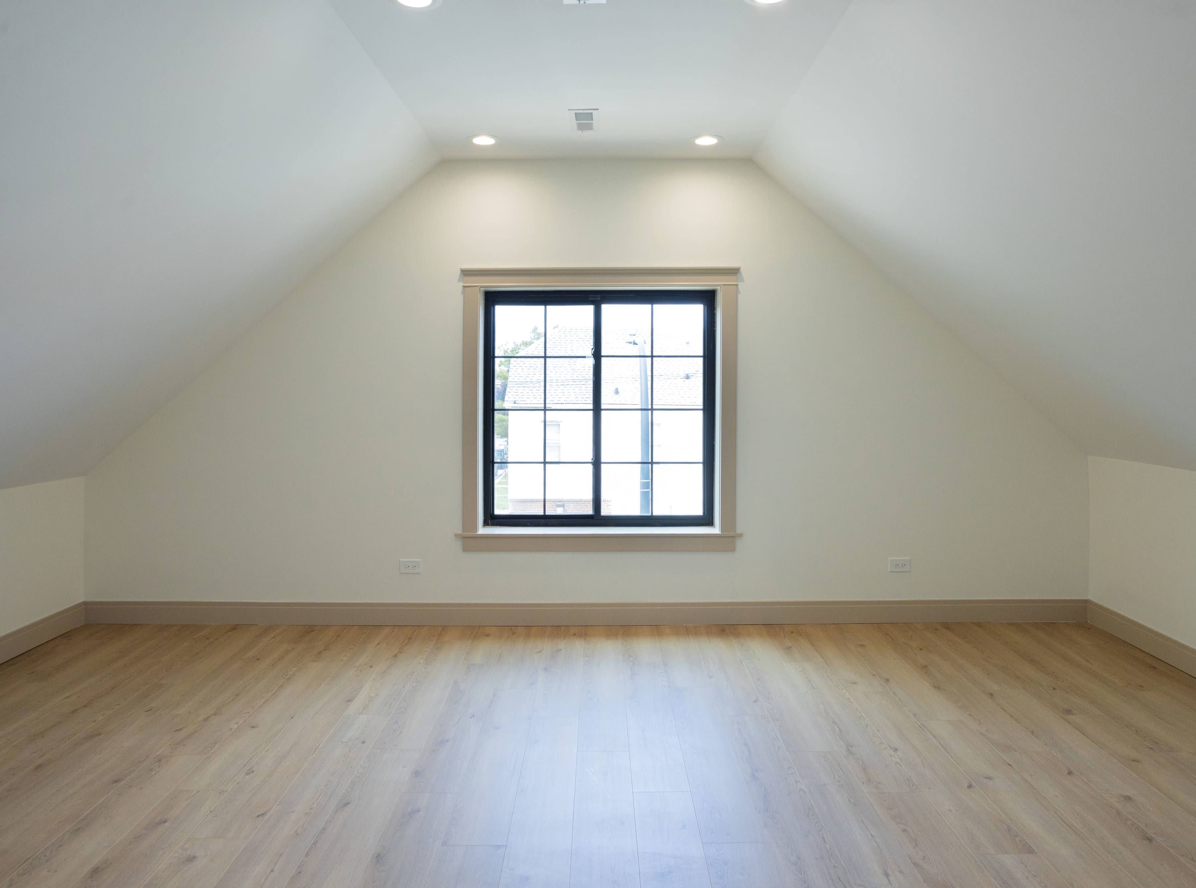 The image shows a spacious, empty attic with sloped ceilings and a large window.